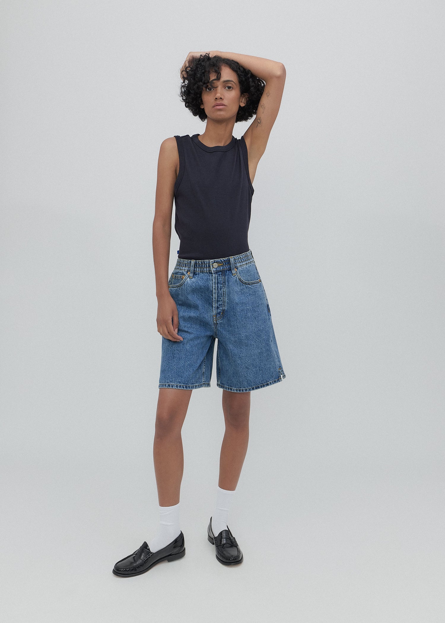 Person wearing a black sleeveless top and blue denim shorts on a plain background