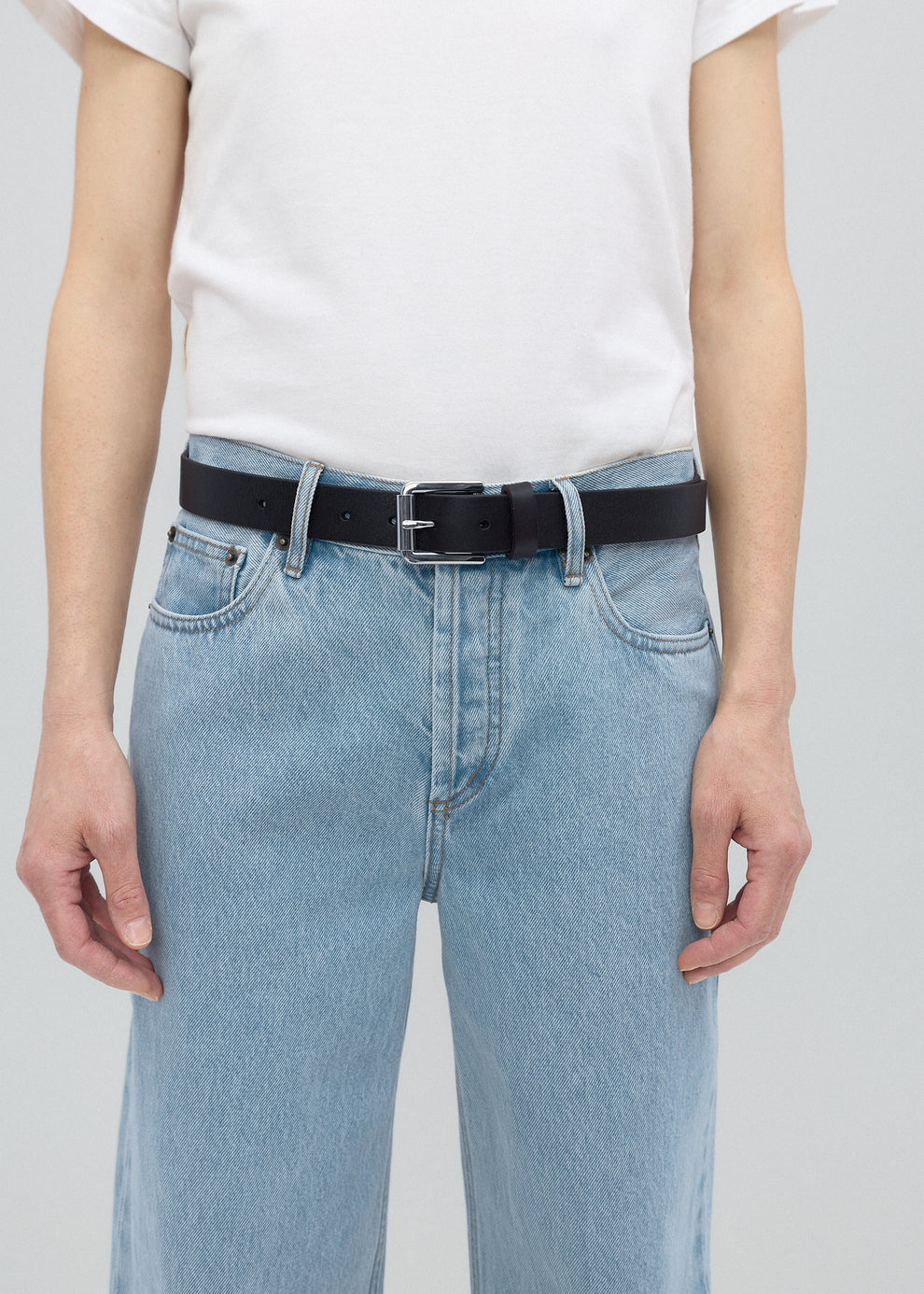 Person wearing light blue jeans and a black belt on a plain background