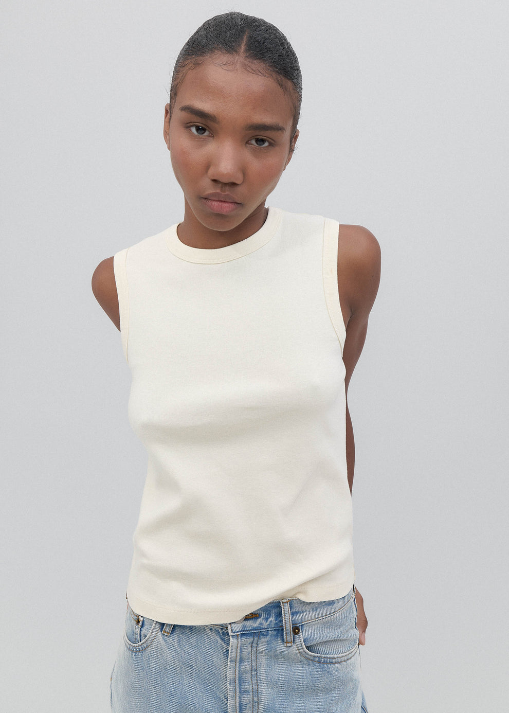 Person wearing a white sleeveless top and blue jeans on a plain background