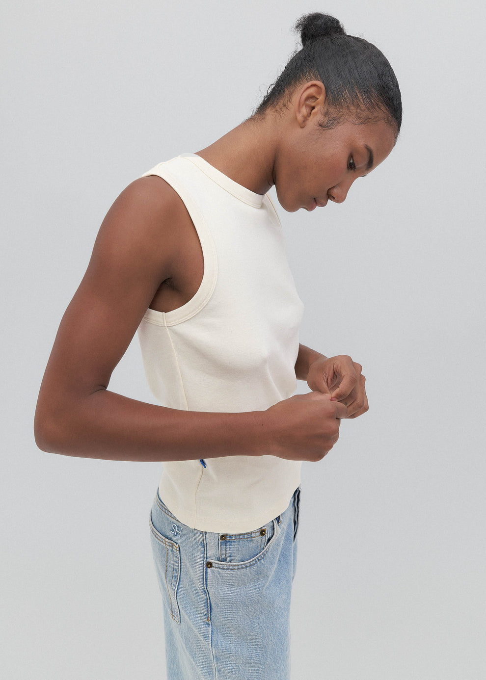 Woman wearing a white sleeveless top and light blue jeans against a plain background