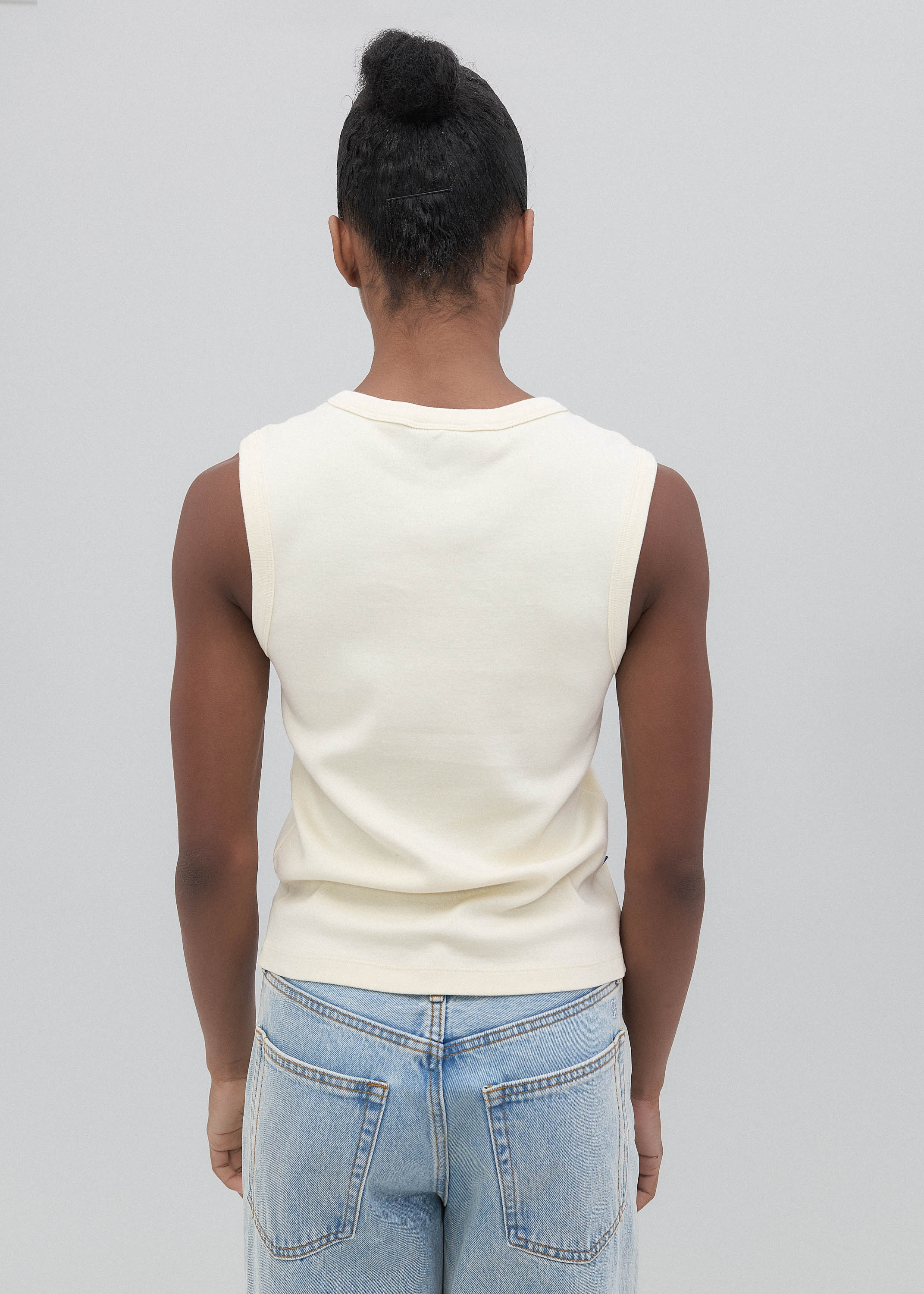 Person wearing a white sleeveless top and blue jeans on a plain background