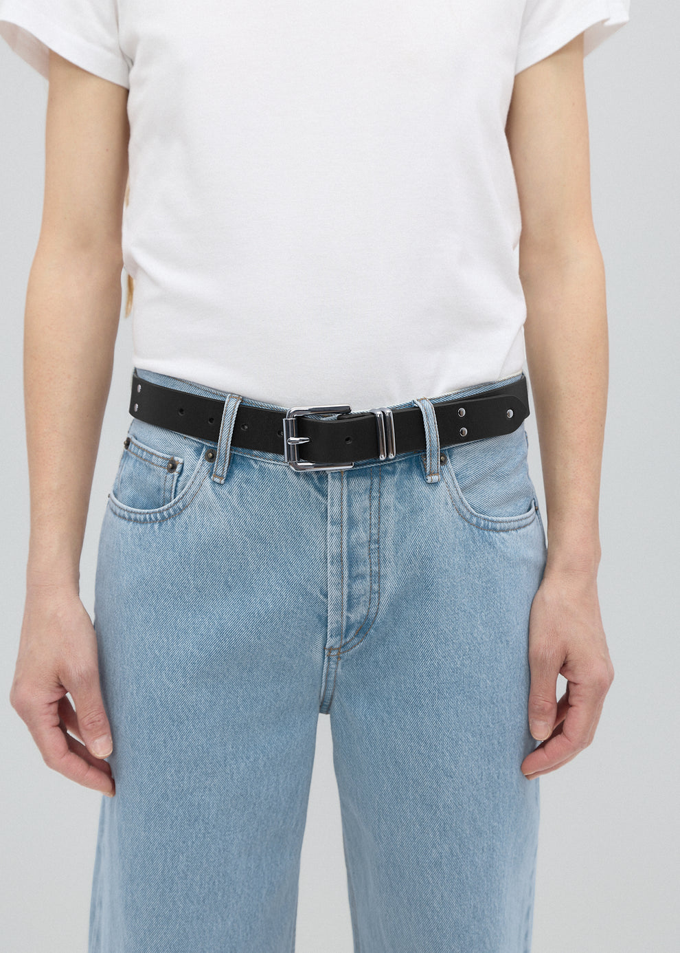 Person wearing light blue jeans and a black belt on a plain background