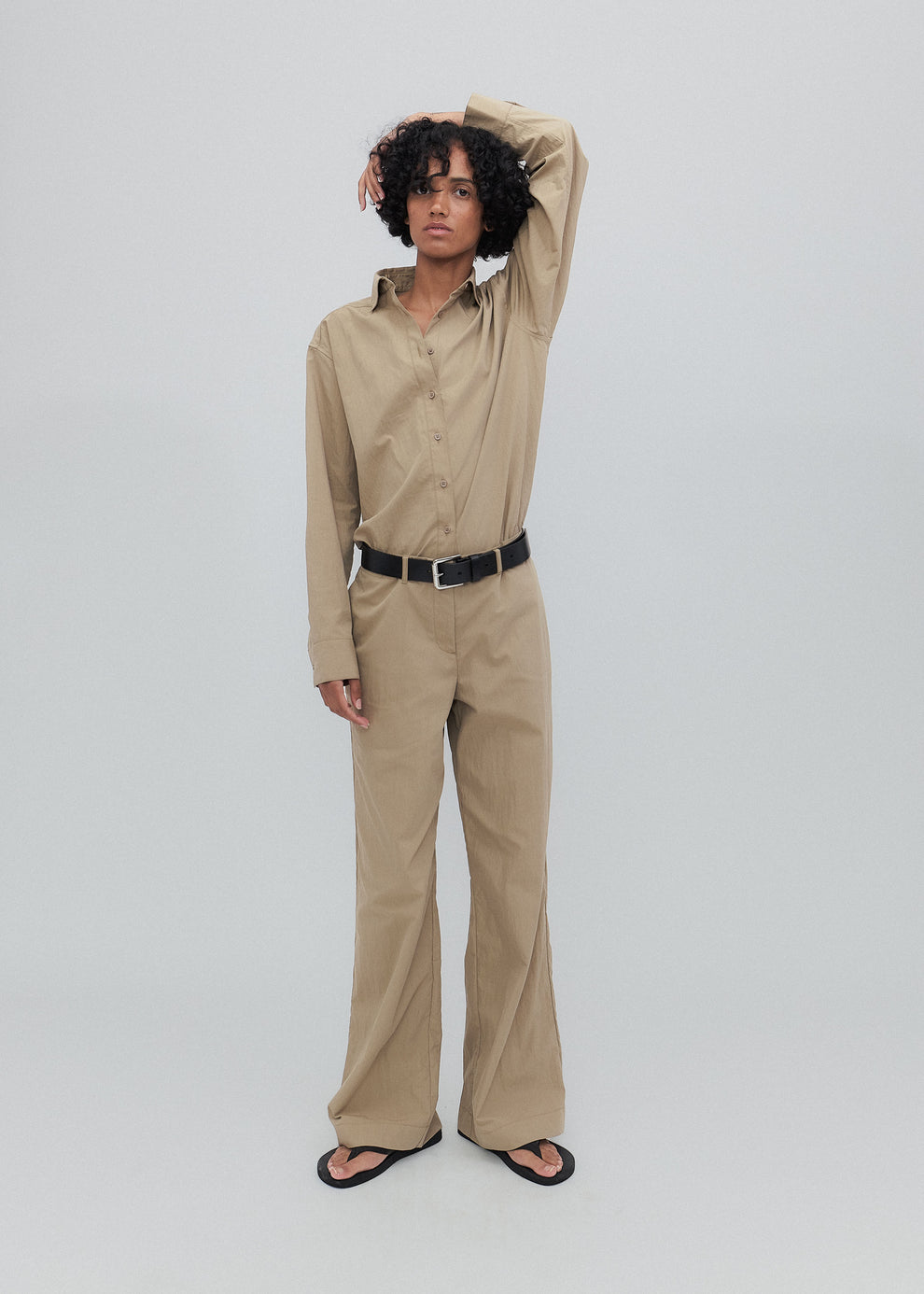 Person wearing a beige shirt and pants with a black belt on a white background