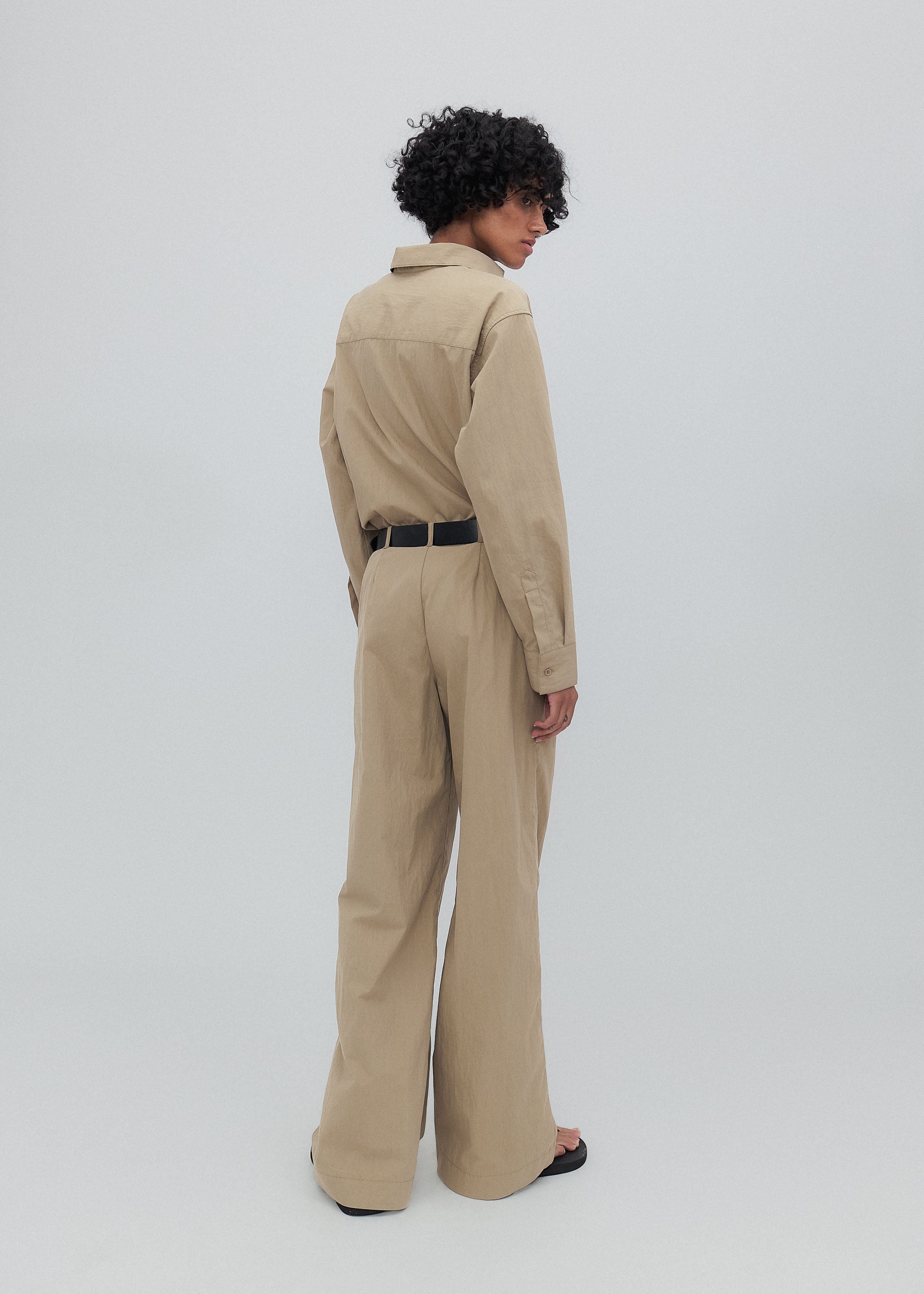 Person wearing a beige jumpsuit on a light gray background