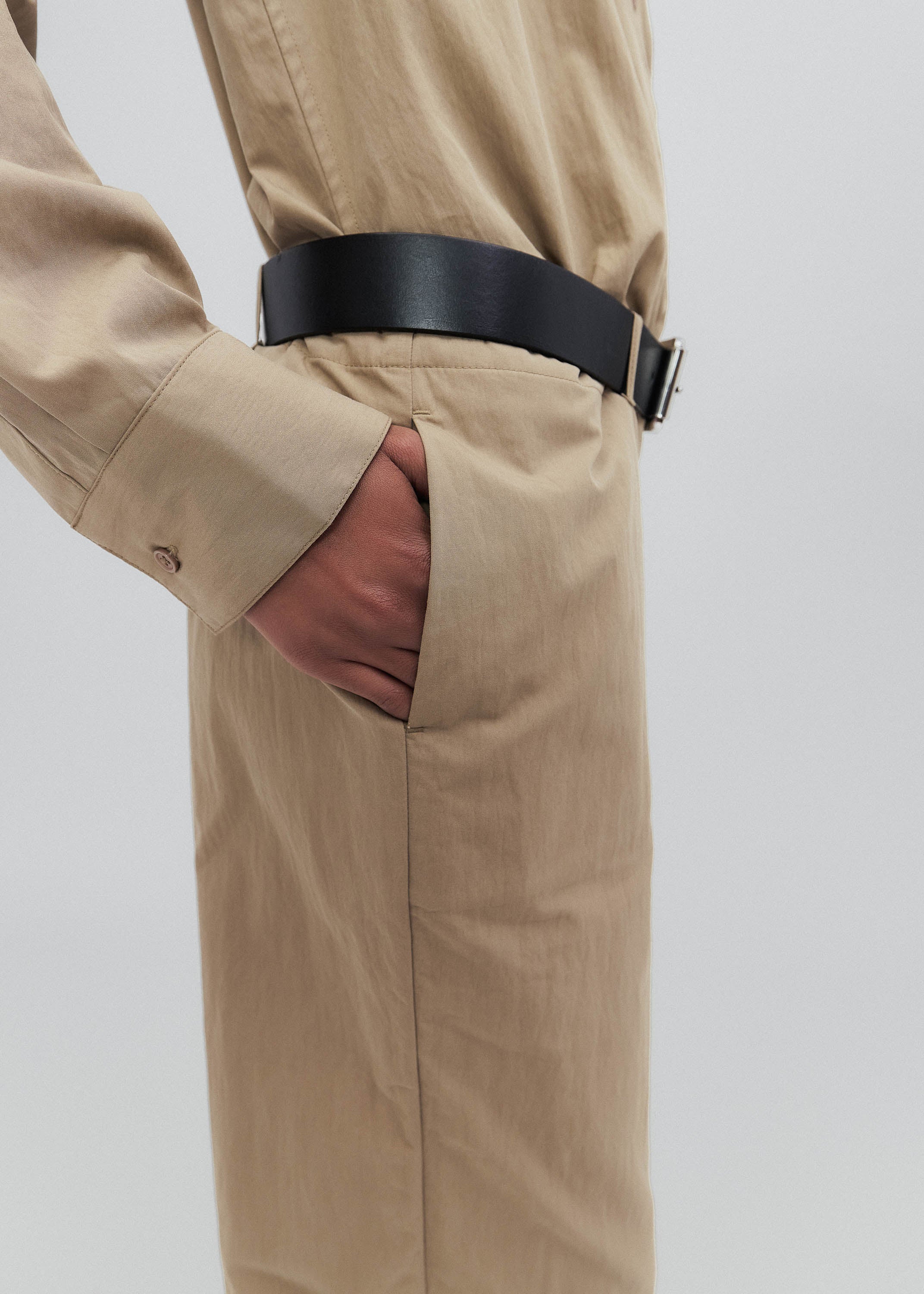 Beige trench coat with a black belt on a white background