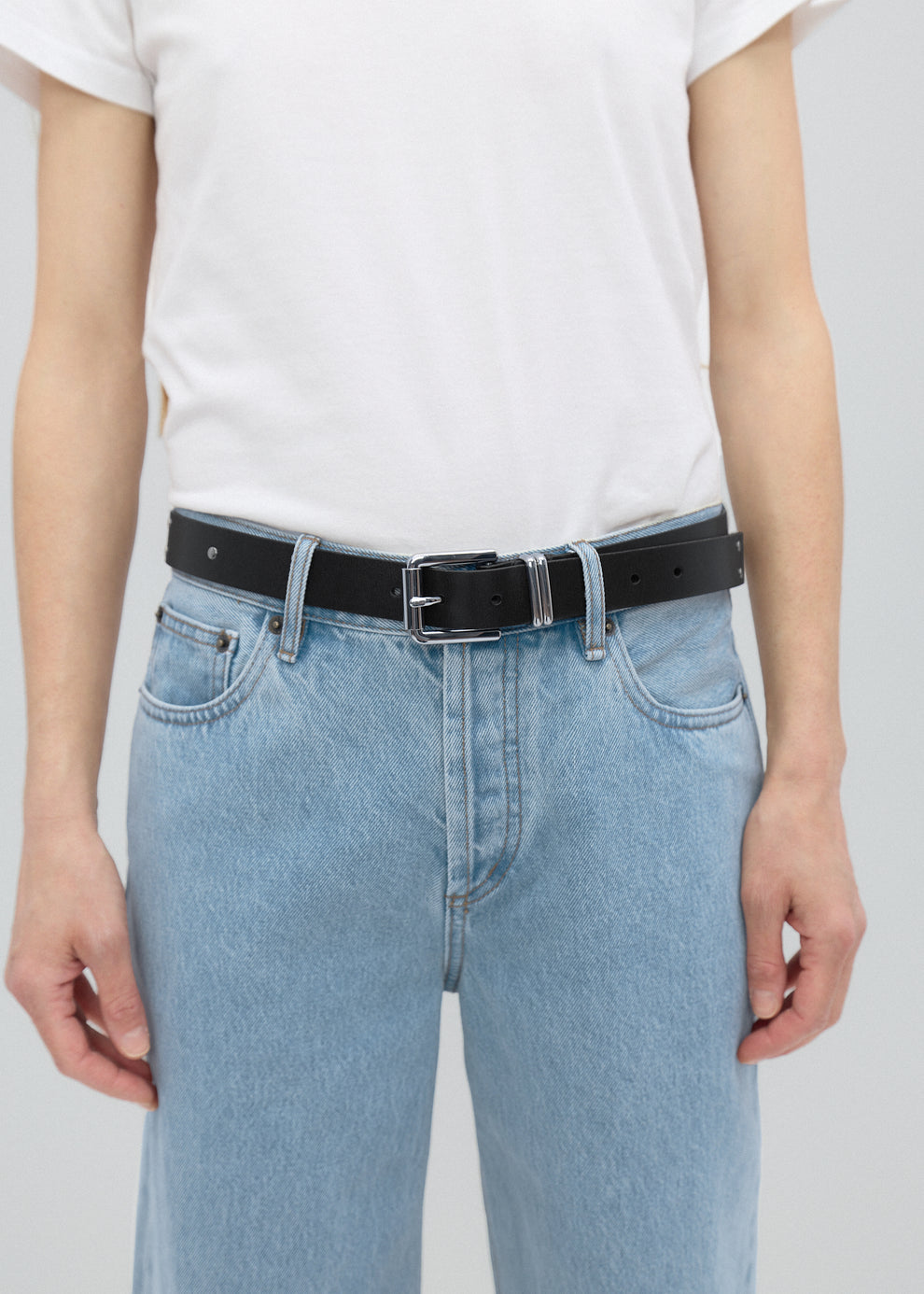 Person wearing light blue jeans and a black belt on a plain background