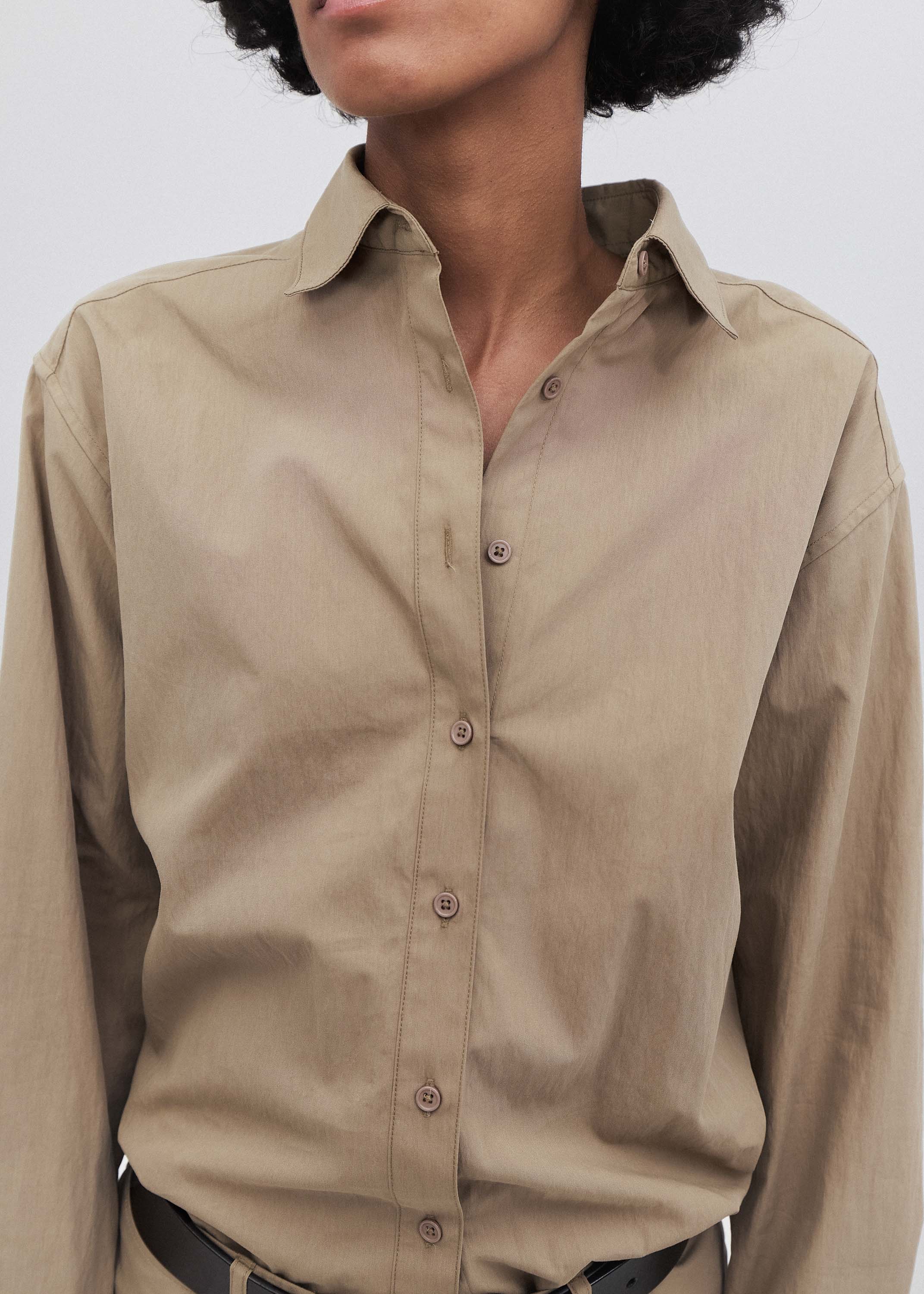 Beige button-up shirt worn by a person on a white background