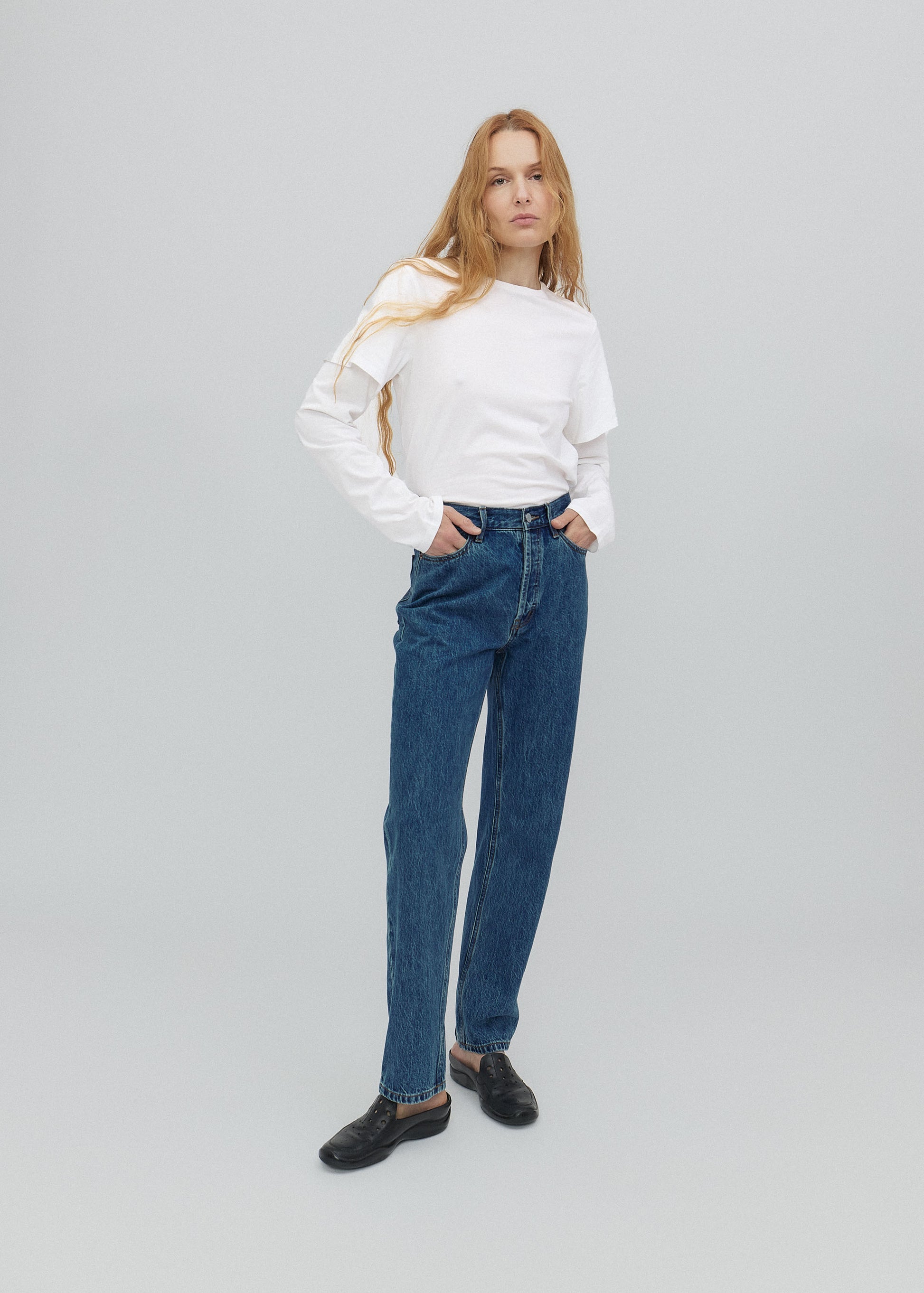 Woman wearing a white sweater and blue jeans on a gray background