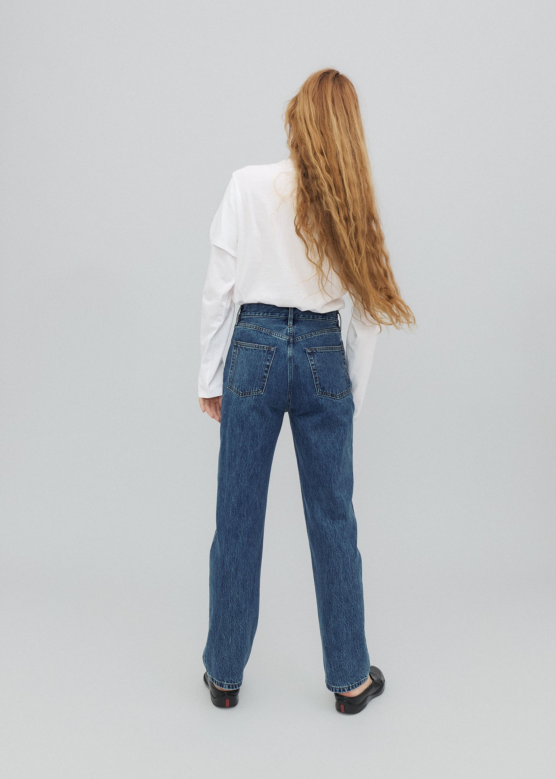 Person wearing blue jeans and a white shirt from behind on a gray background