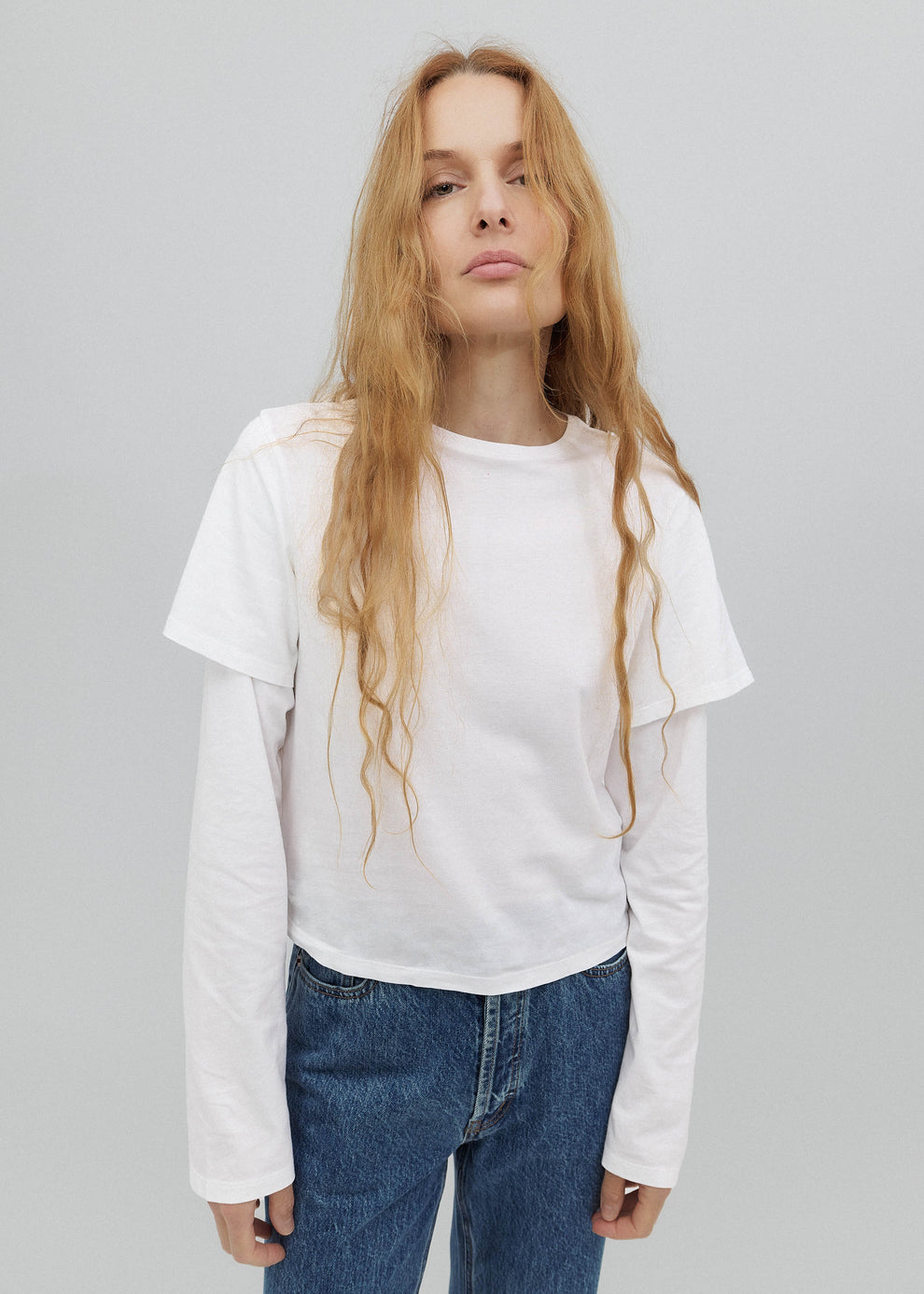 Person wearing a white long-sleeve shirt and blue jeans on a gray background