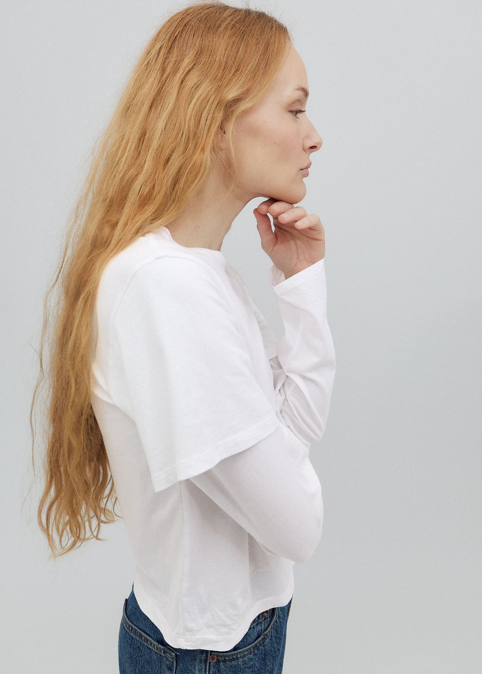 Woman wearing a white oversized shirt and blue jeans against a light gray background