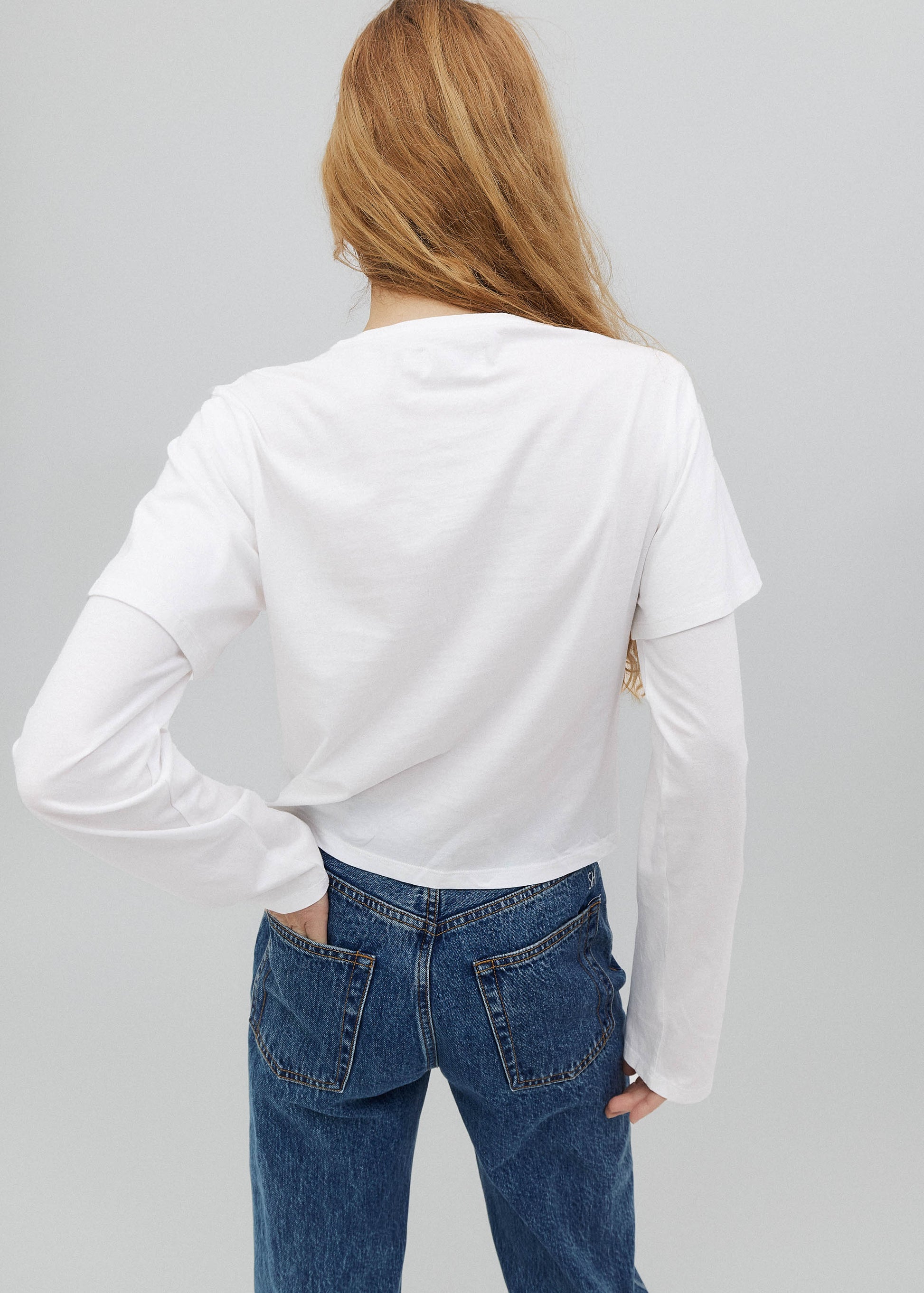 Person wearing a white long-sleeve shirt and blue jeans on a gray background