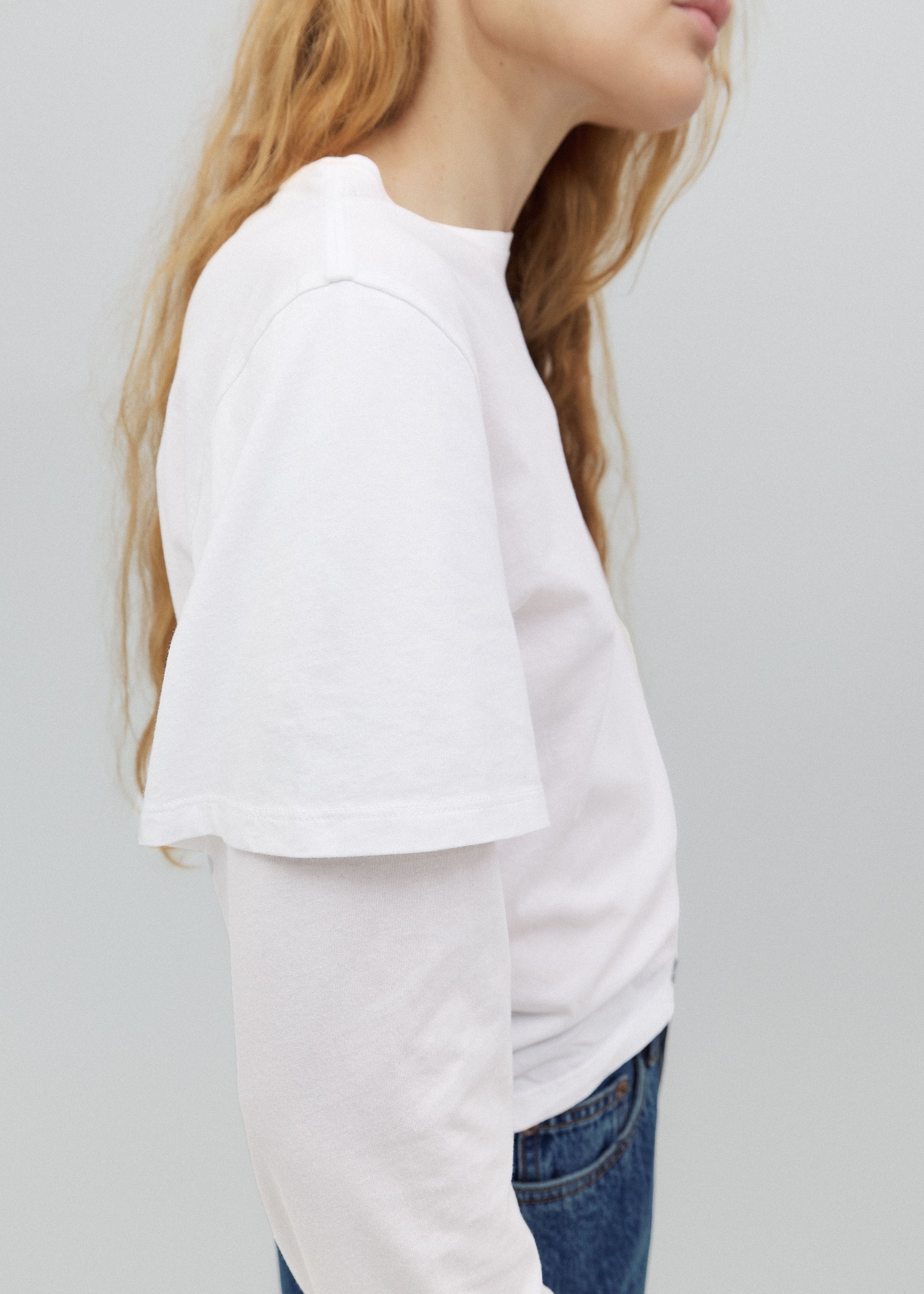 Person wearing a white oversized t-shirt and blue jeans on a plain background