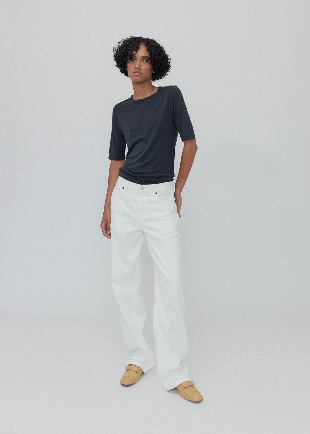 Person wearing a black t-shirt and white pants on a light gray background