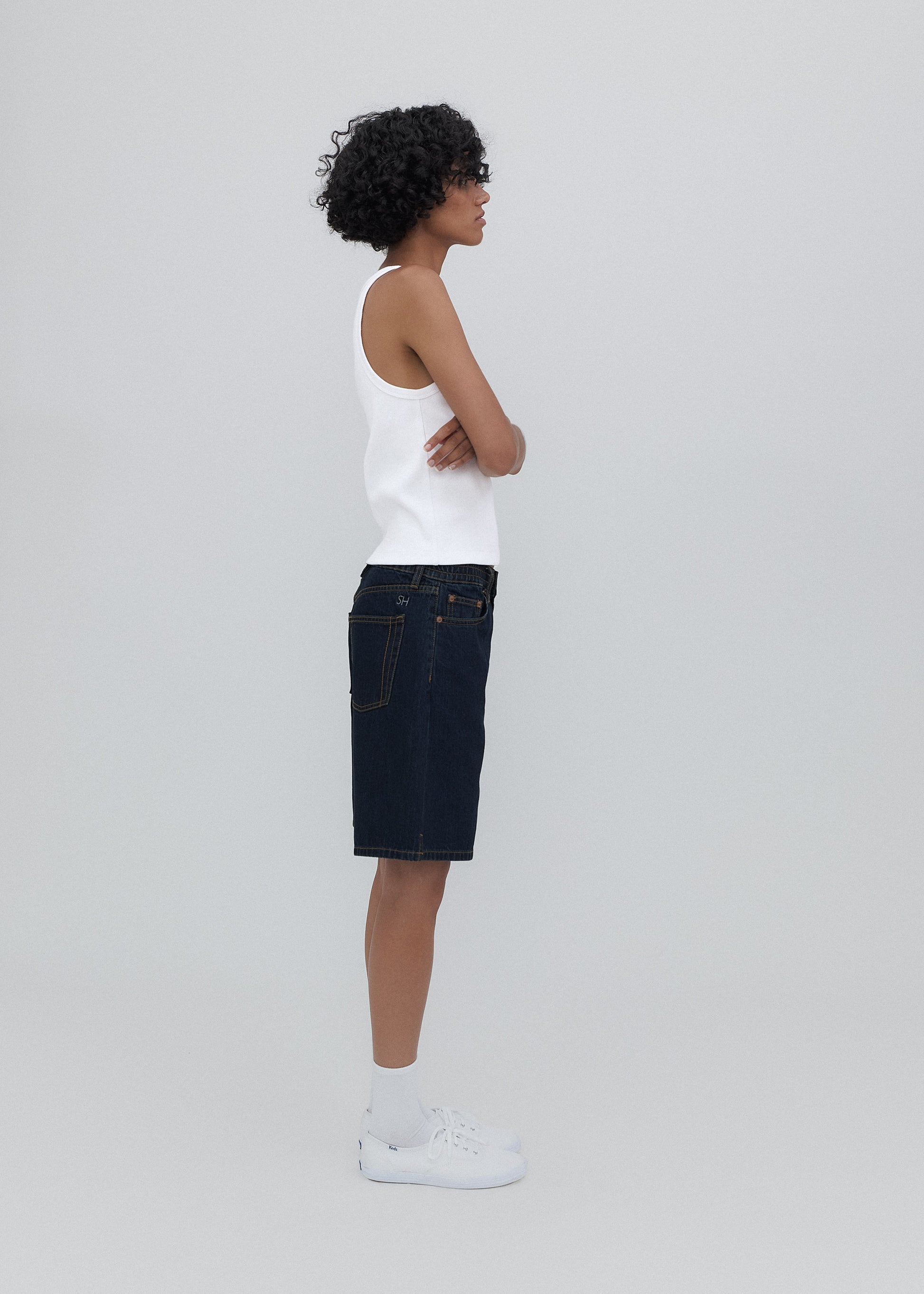 Person wearing a white tank top and dark denim skirt on a plain background