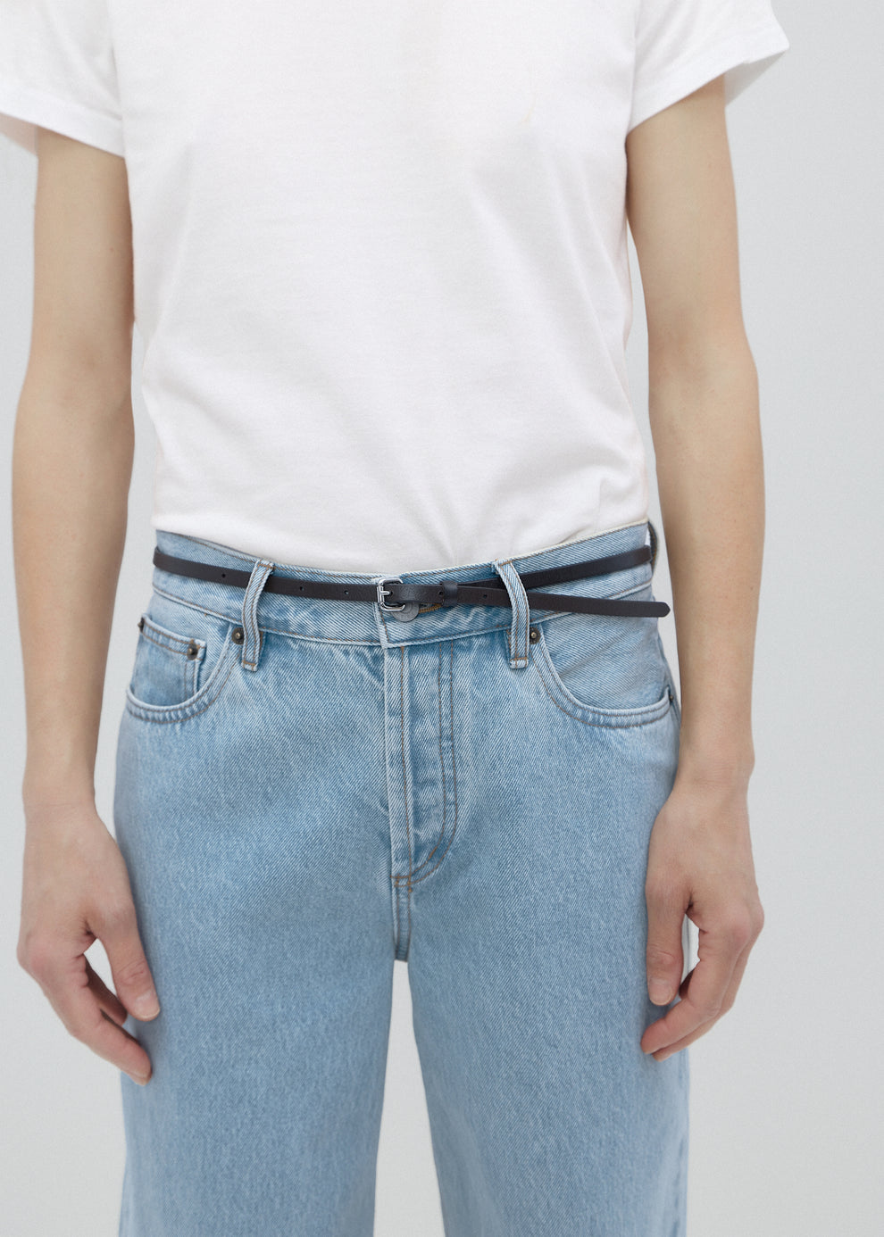 Person wearing light blue jeans and a white t-shirt on a plain background