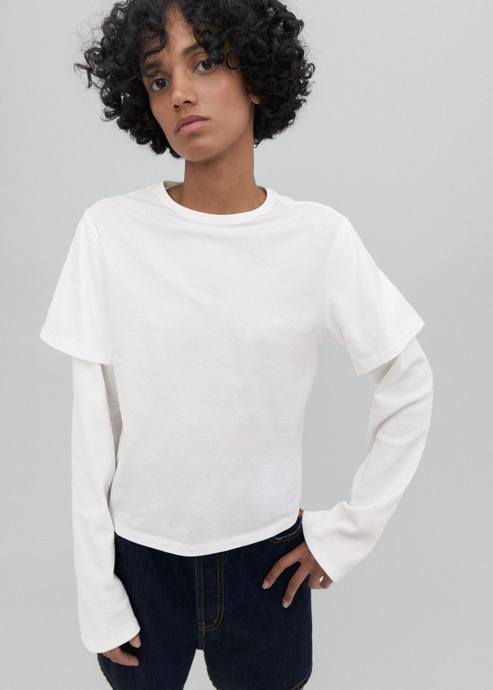 Person wearing a white long-sleeve shirt and dark jeans on a gray background