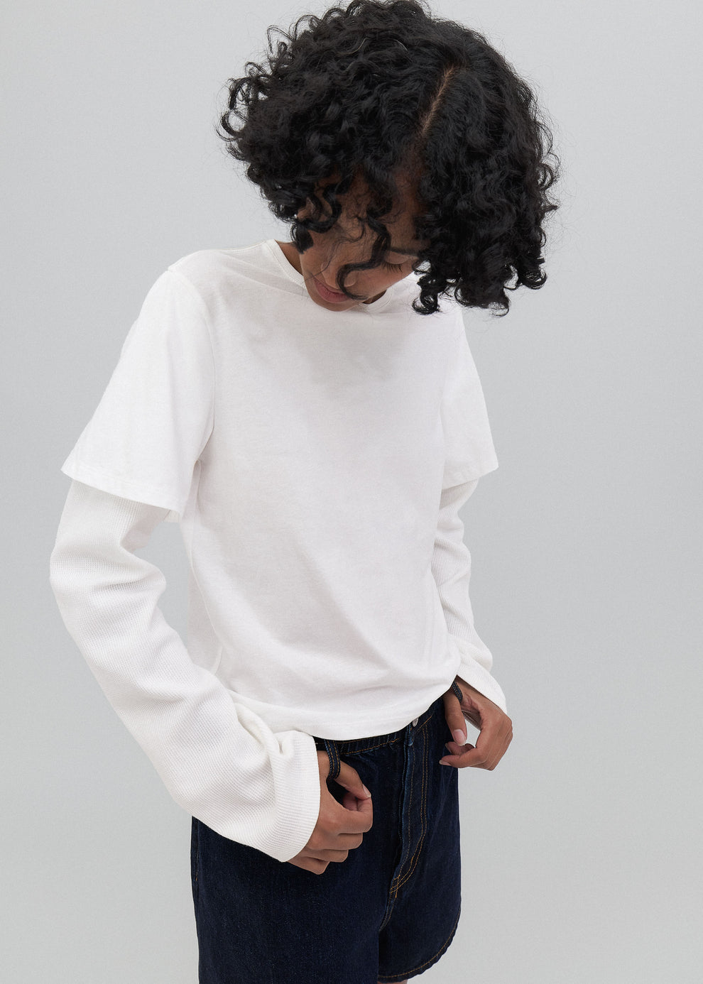 Person wearing a white long-sleeve shirt and dark pants on a gray background