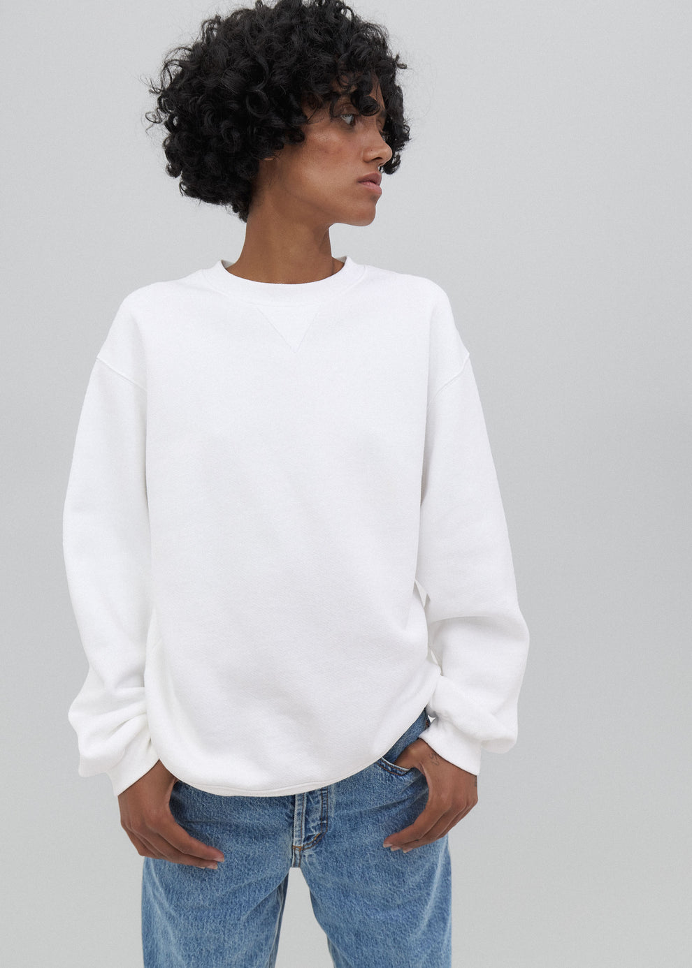 Person wearing a white sweatshirt and blue jeans on a gray background