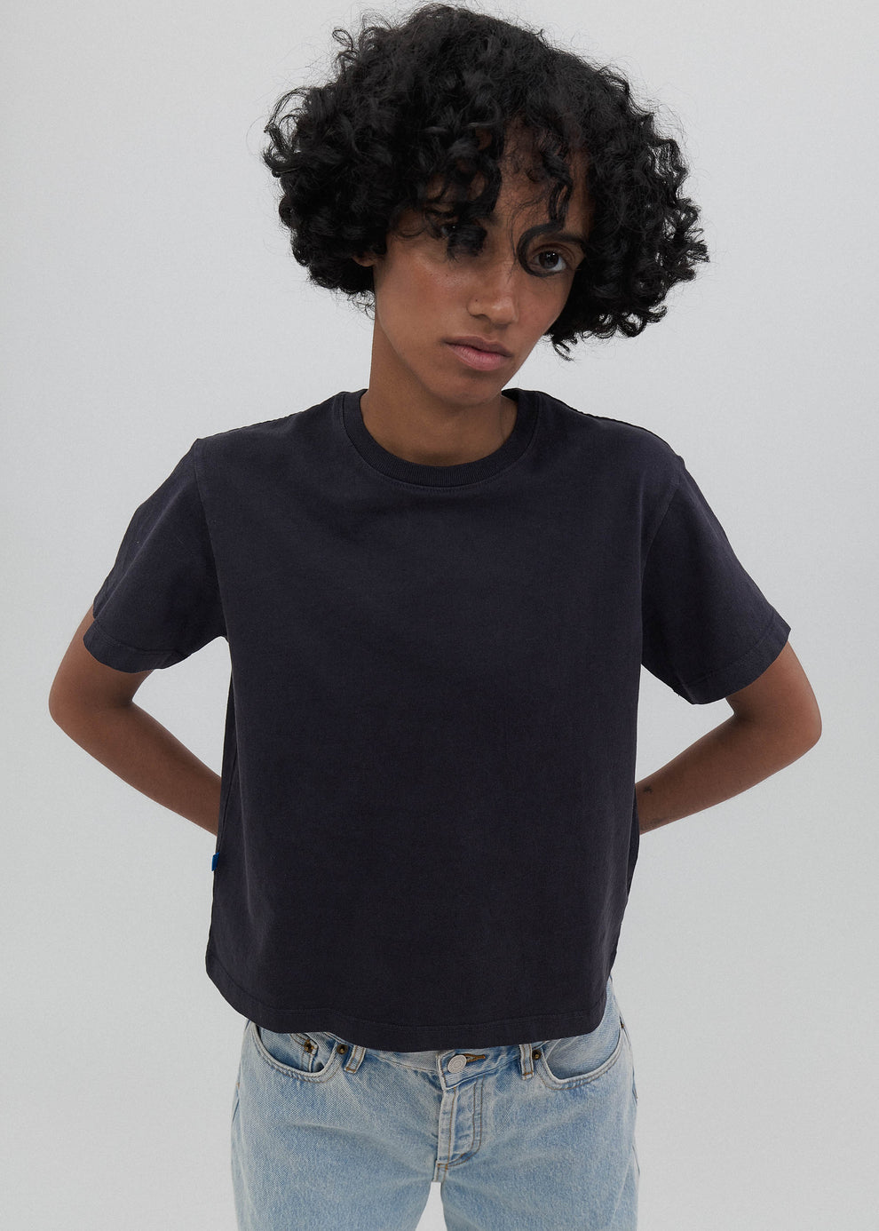 Person wearing a black t-shirt and light blue jeans against a plain background