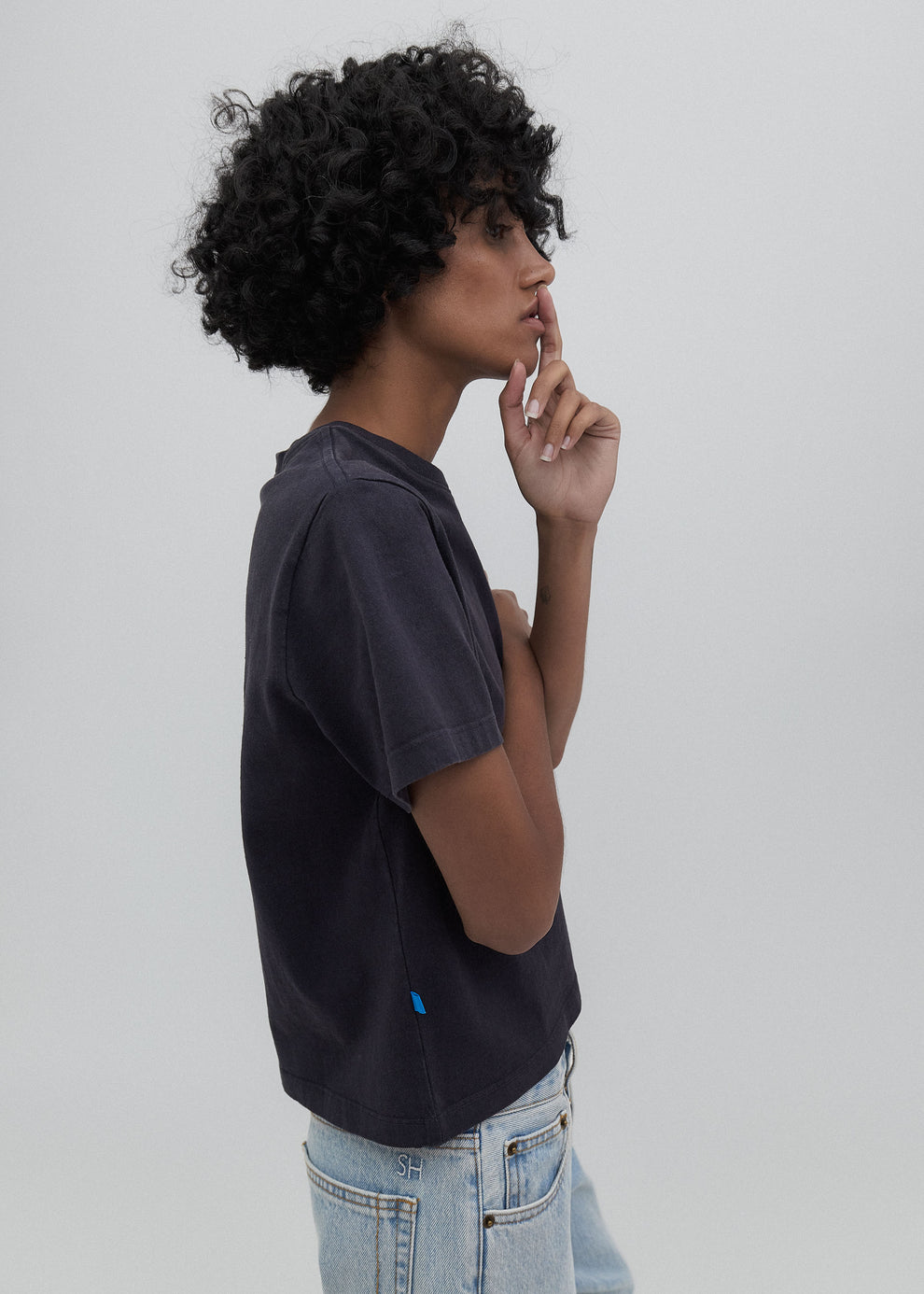 Person wearing a dark gray t-shirt and light blue jeans against a plain background