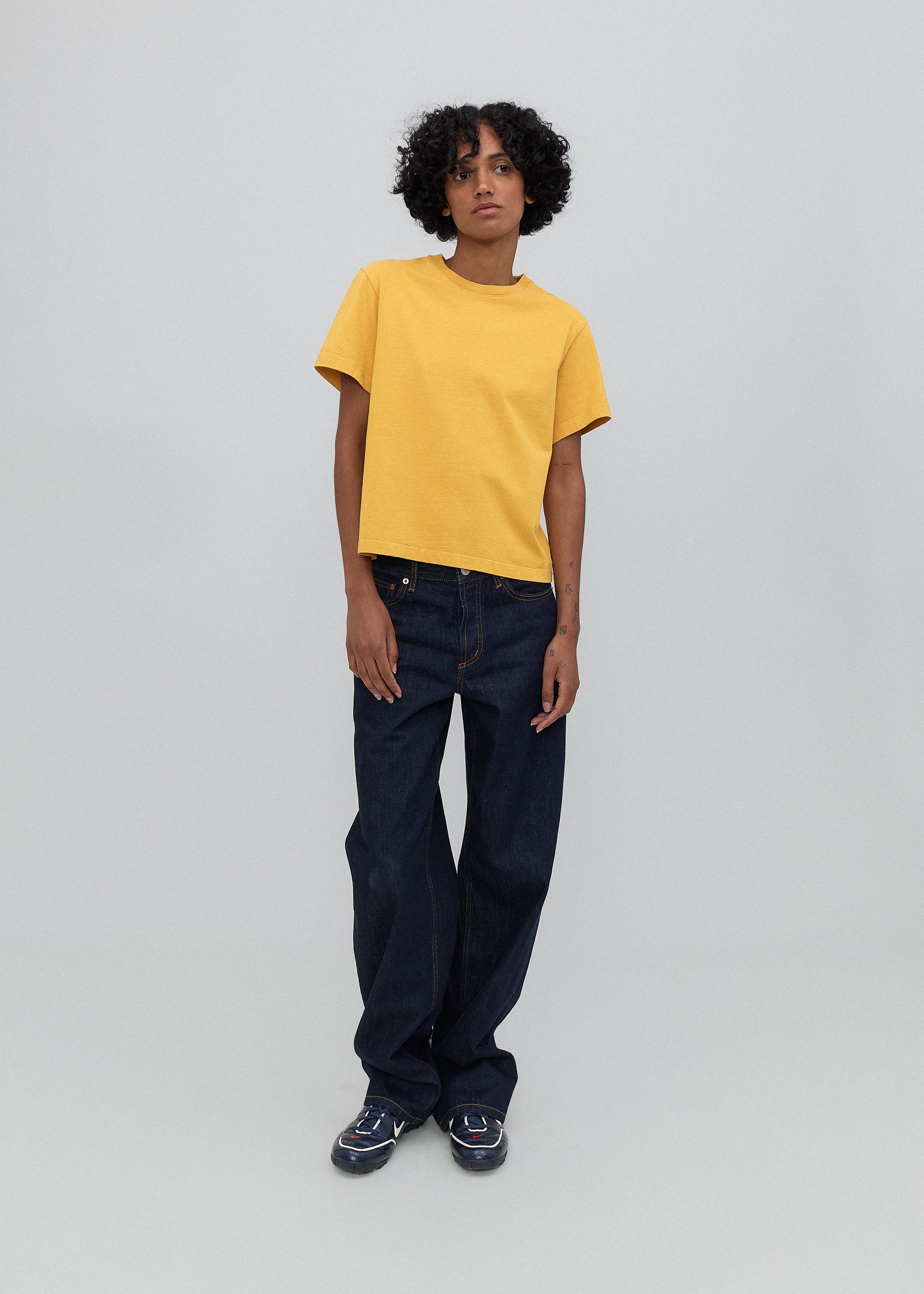 Person wearing a yellow t-shirt and dark blue jeans on a plain background