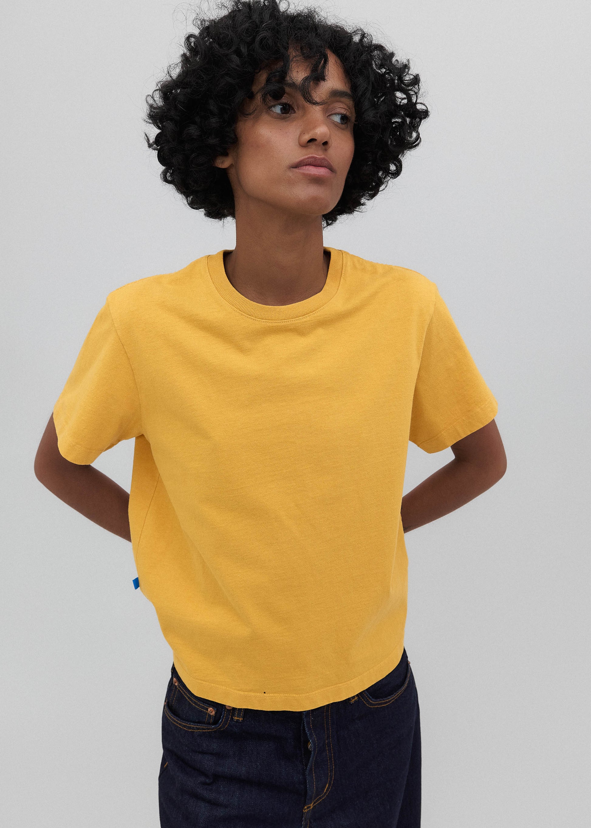 Person wearing a yellow t-shirt and dark jeans against a plain background