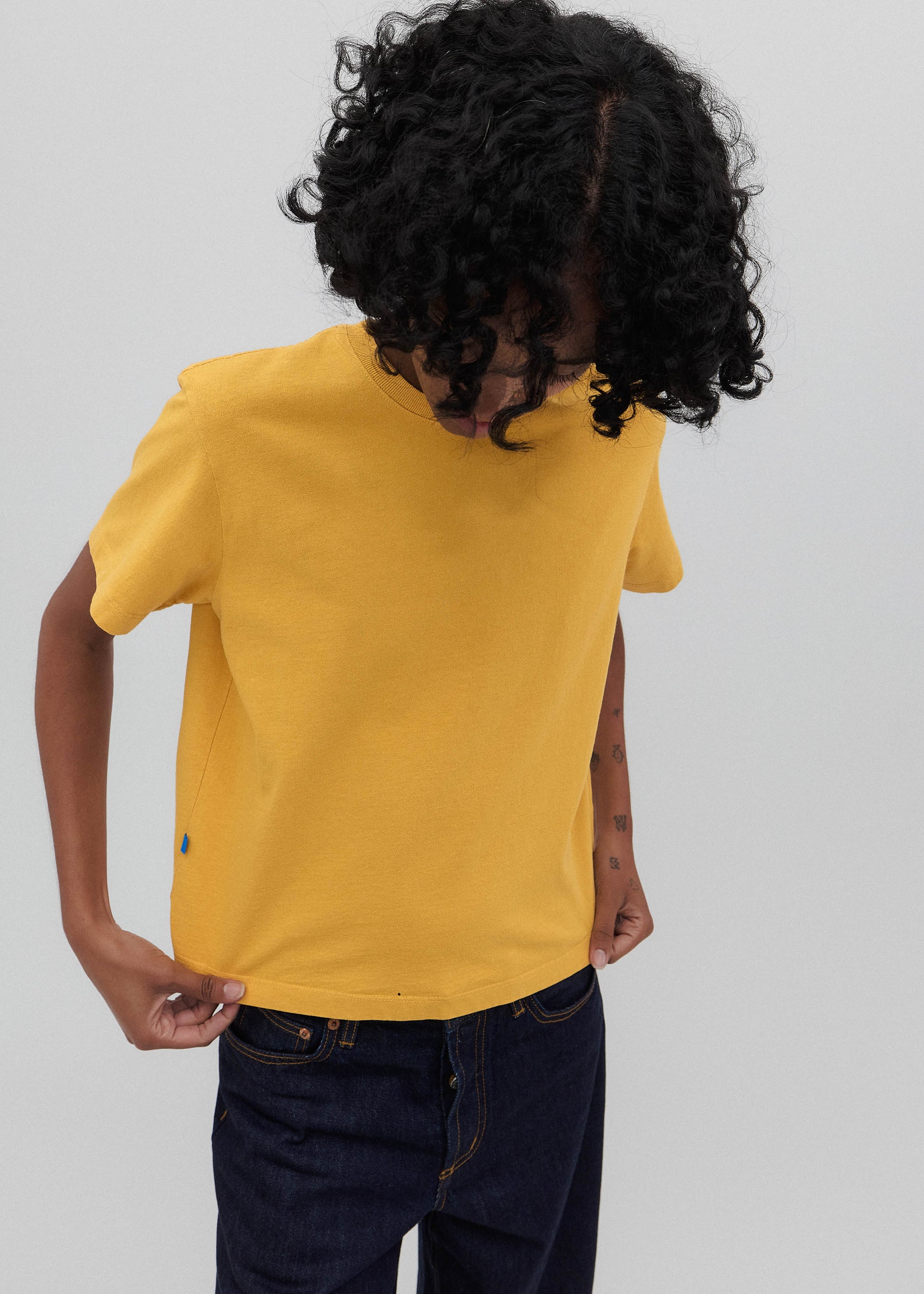 Person wearing a yellow t-shirt and dark jeans on a plain background