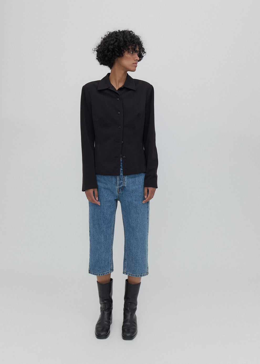 Person wearing a black shirt, blue jeans, and black boots on a white background