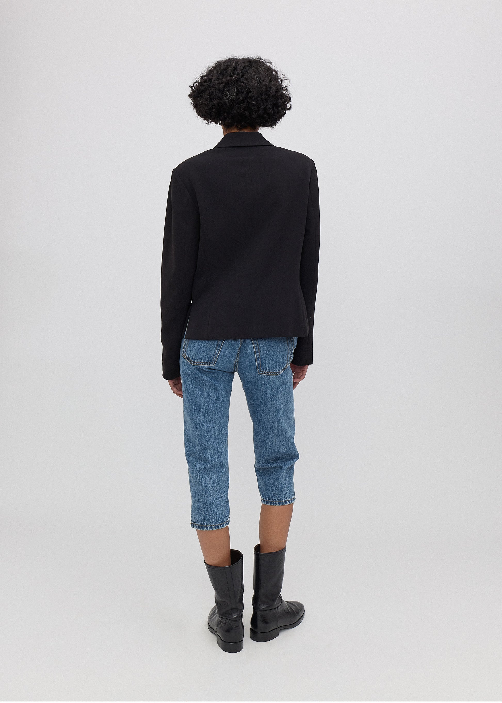 Person wearing a black jacket, blue jeans, and black boots on a white background
