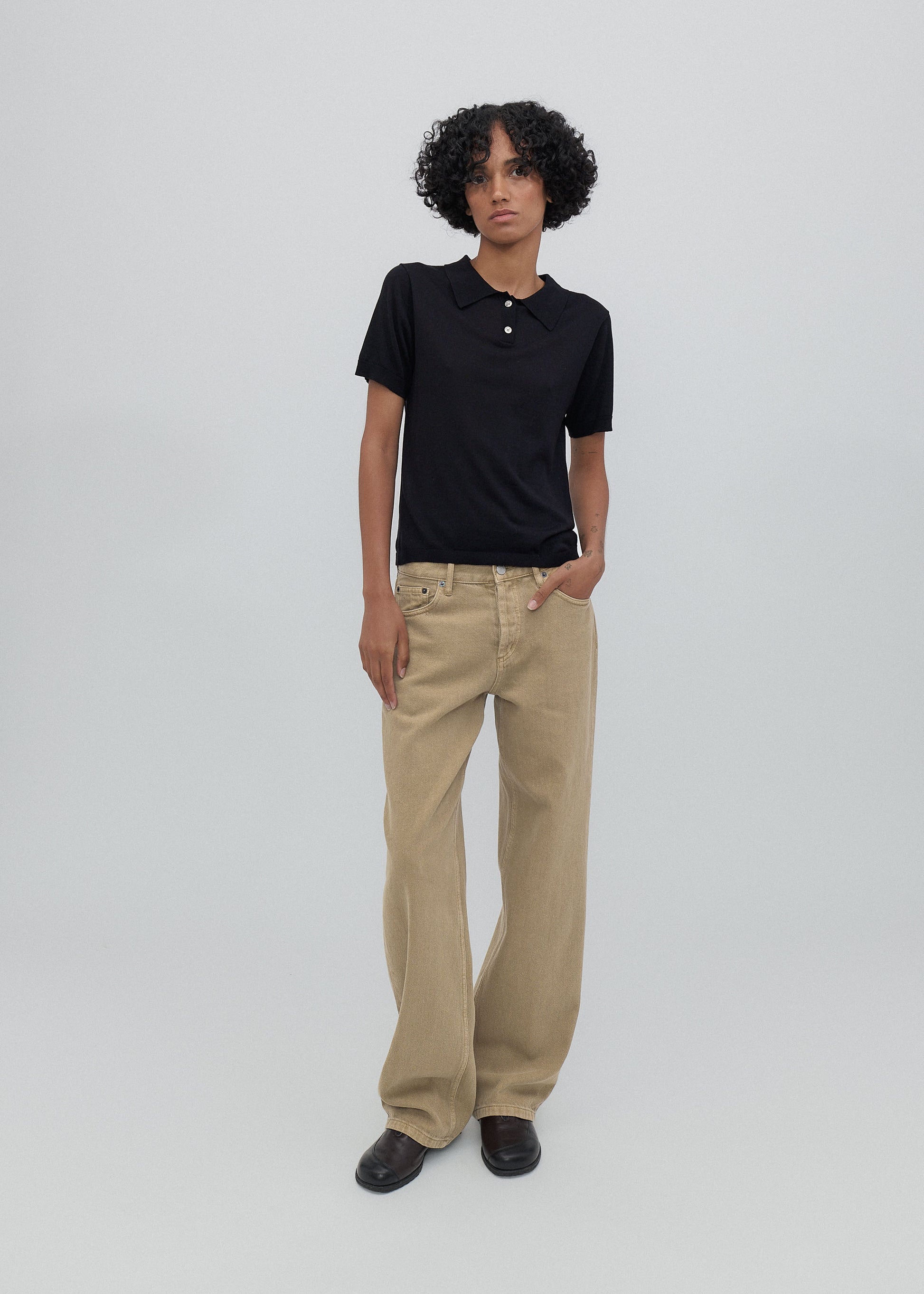 Person wearing a black polo shirt and beige pants on a white background