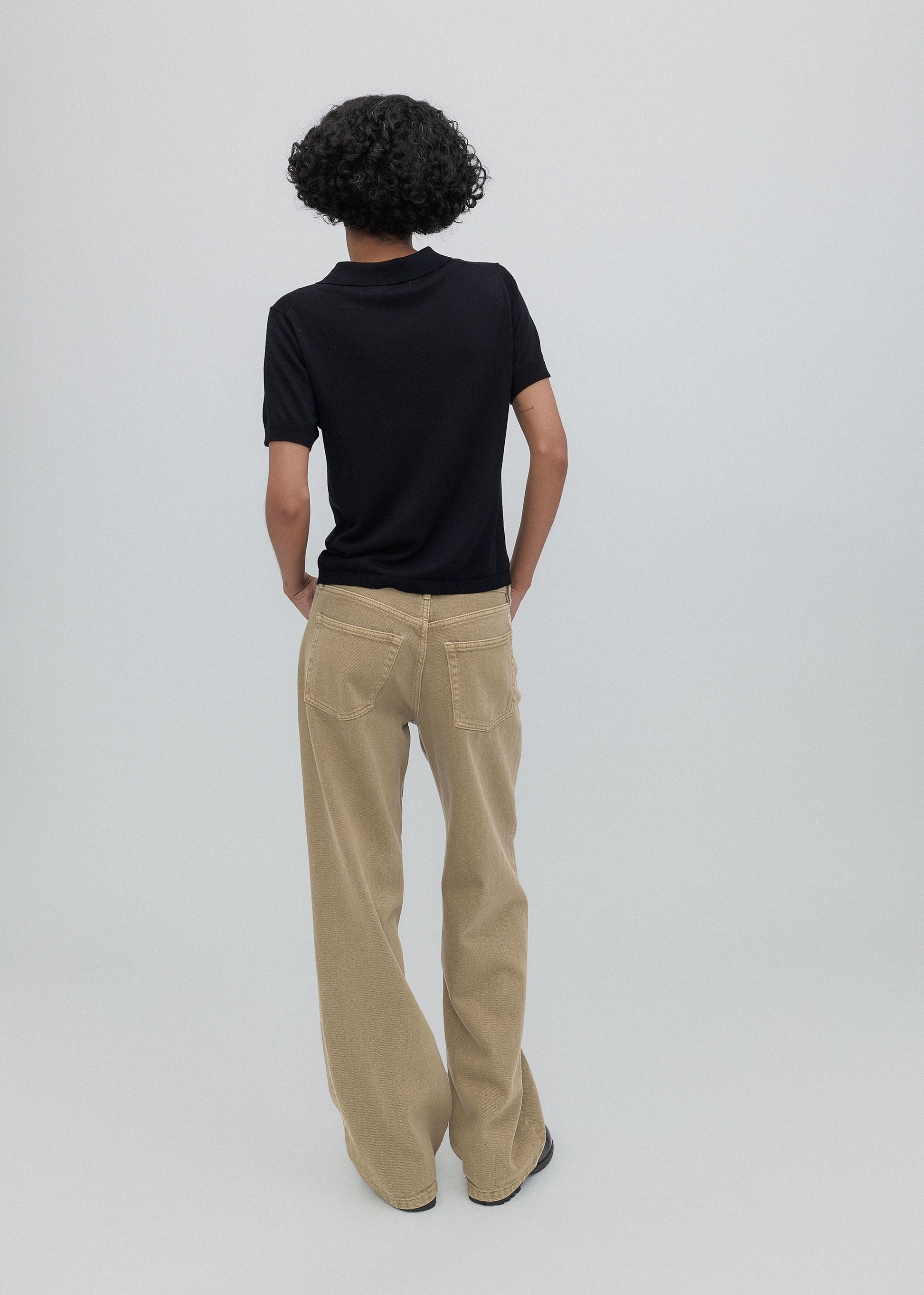 Person wearing a black shirt and beige pants on a plain background