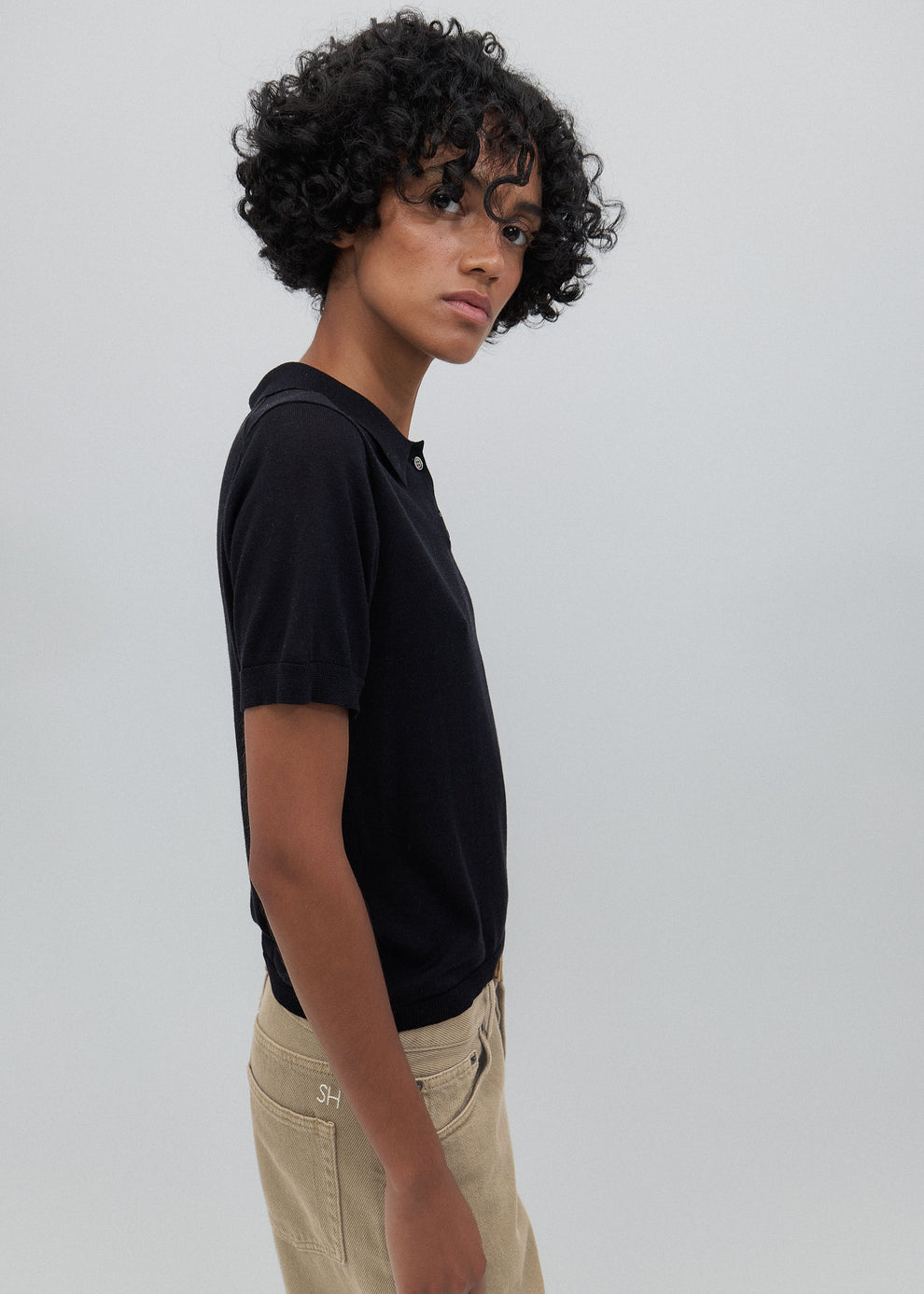 Person wearing a black t-shirt and beige pants against a plain background