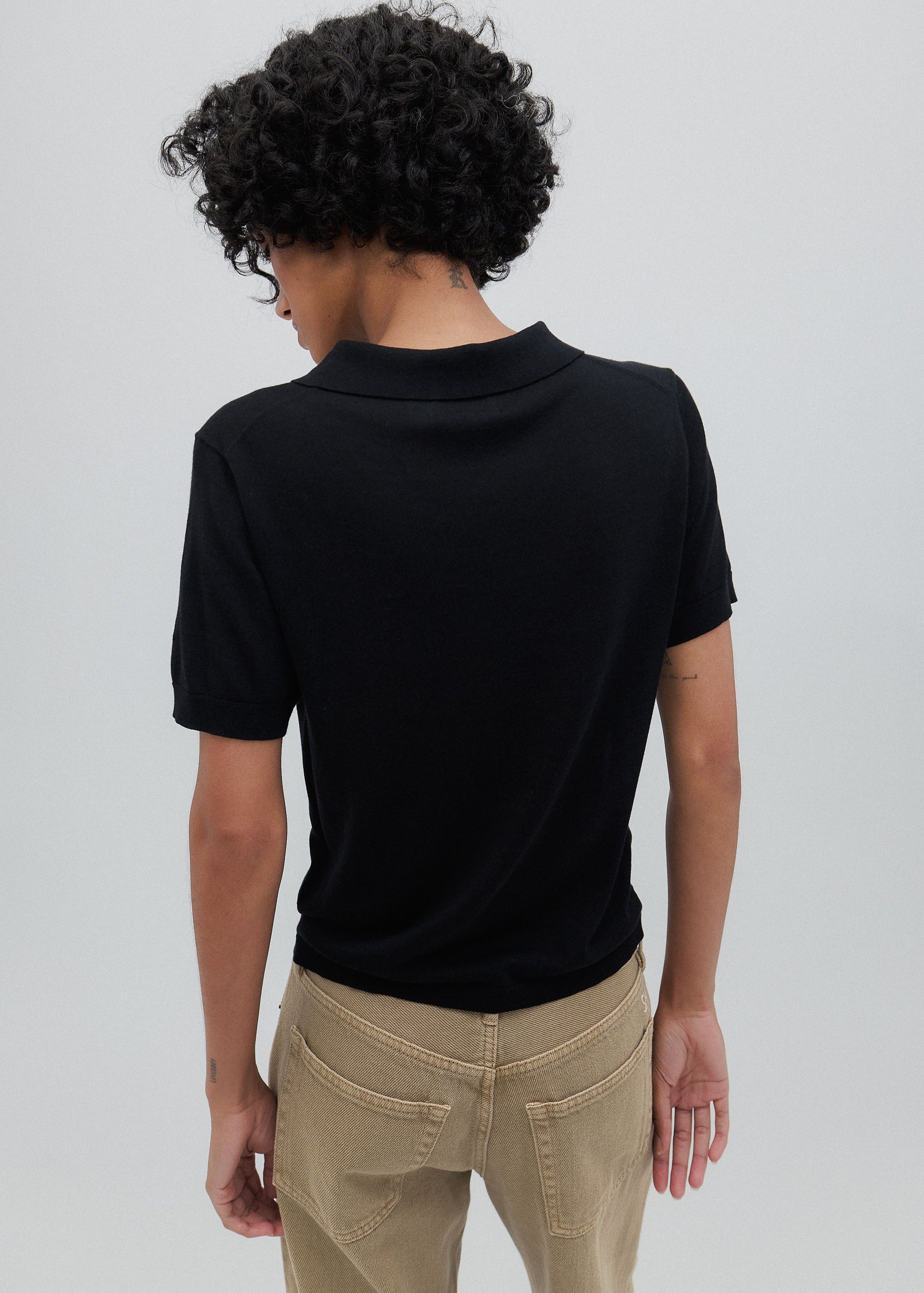 Person wearing a black polo shirt and beige pants against a plain background