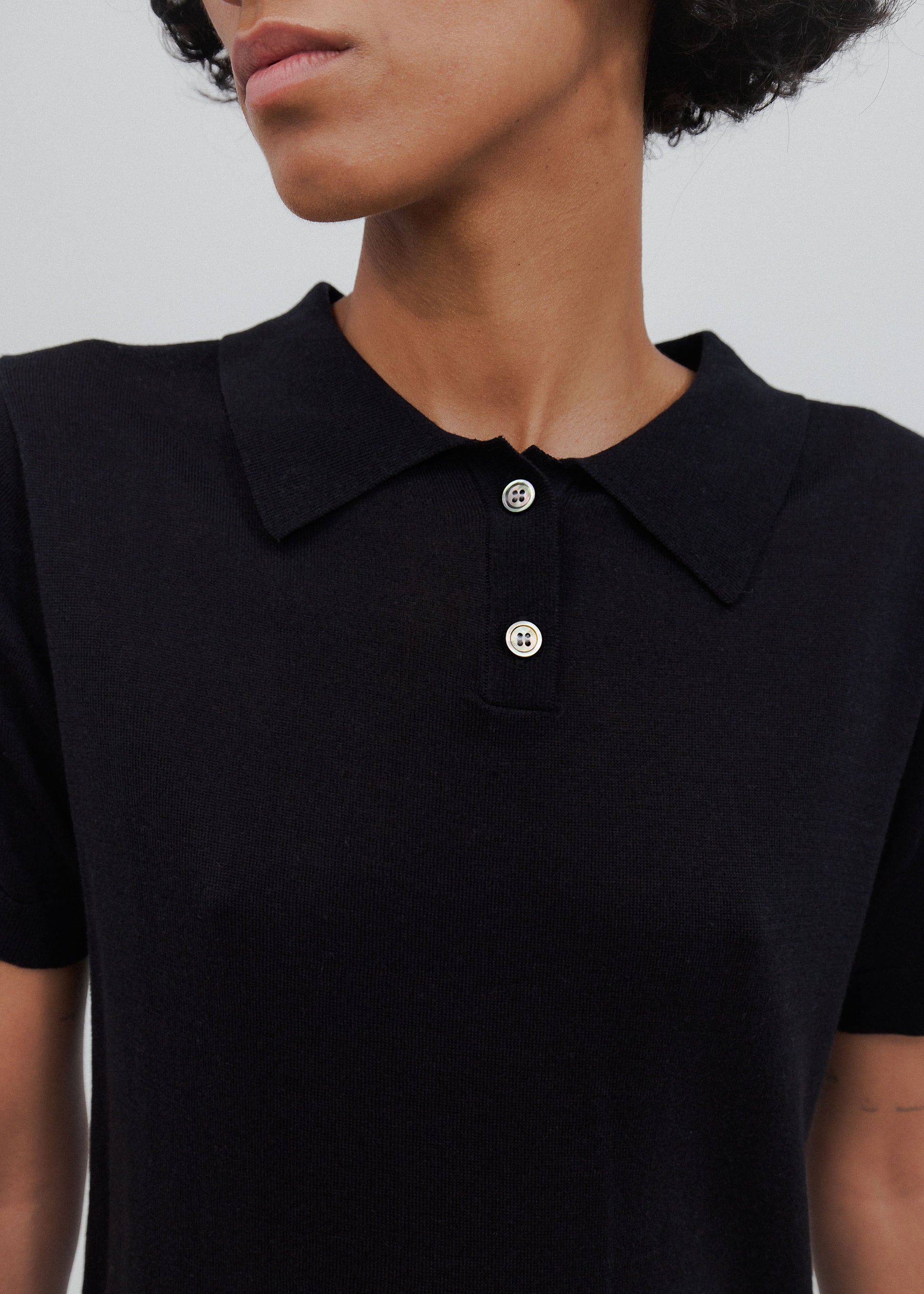 Close-up of a person wearing a black polo shirt with visible buttons on a plain background