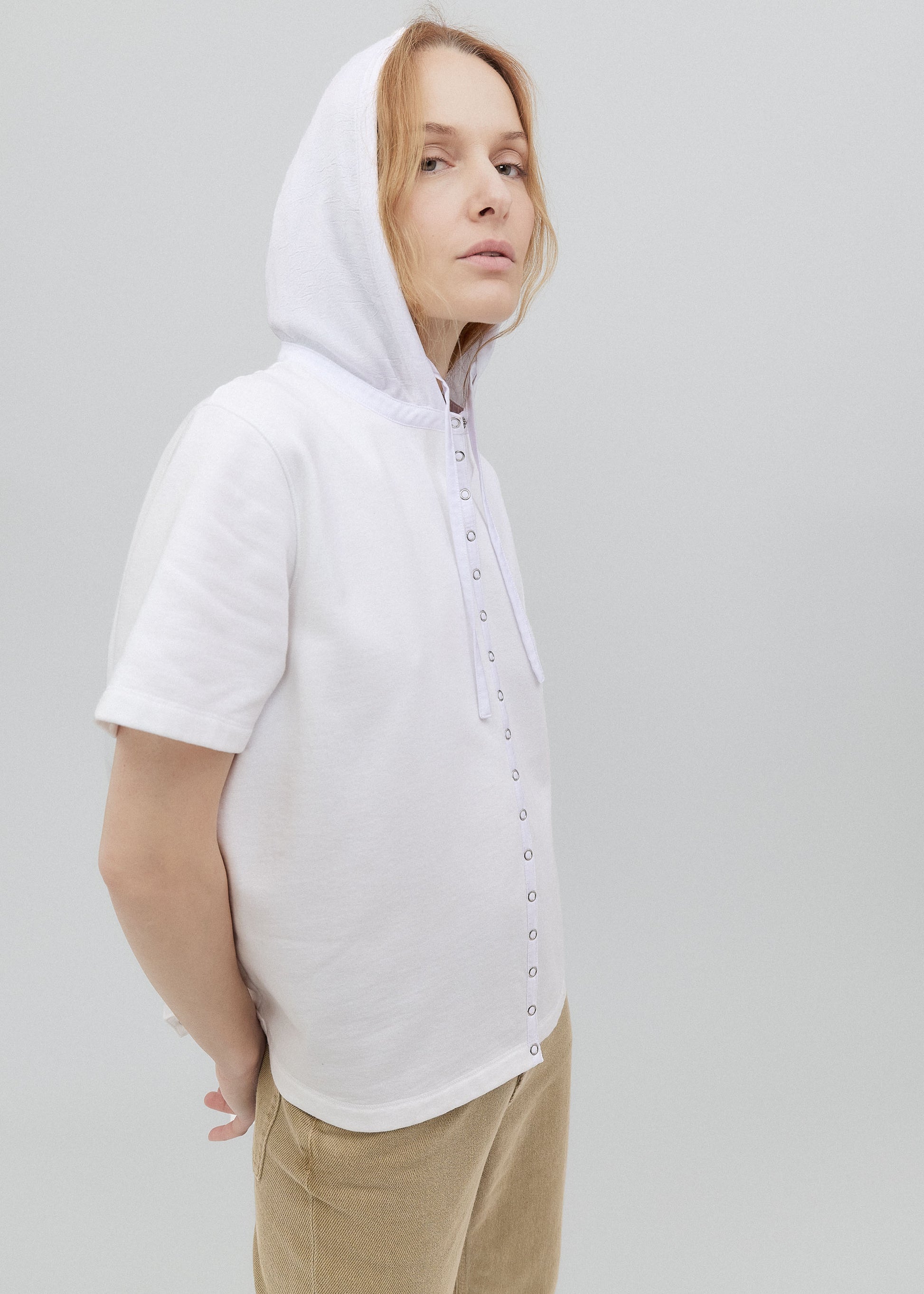 Person wearing a white hoodie with button details on a plain background