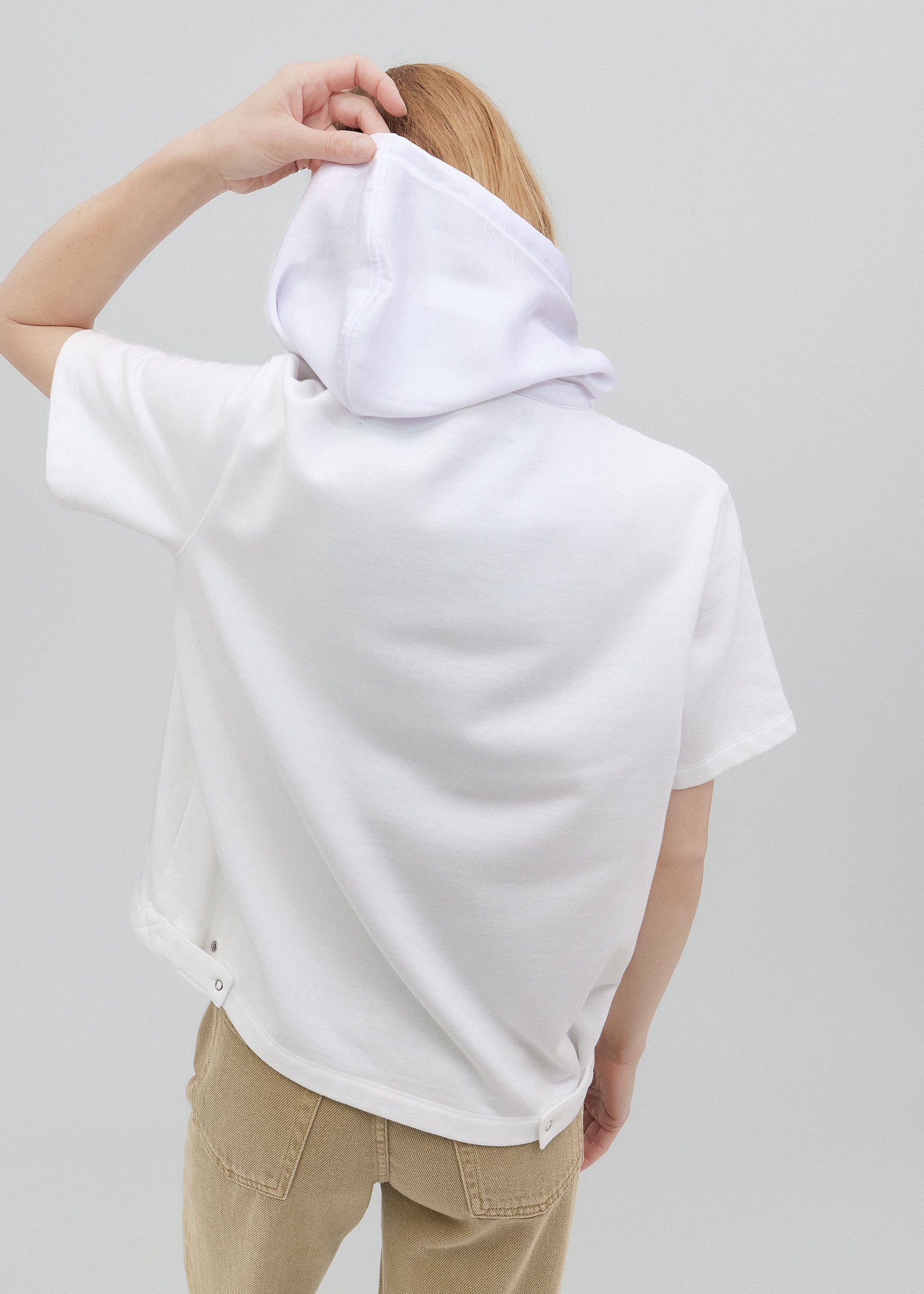 Person wearing a white hoodie with the back facing the camera on a plain background