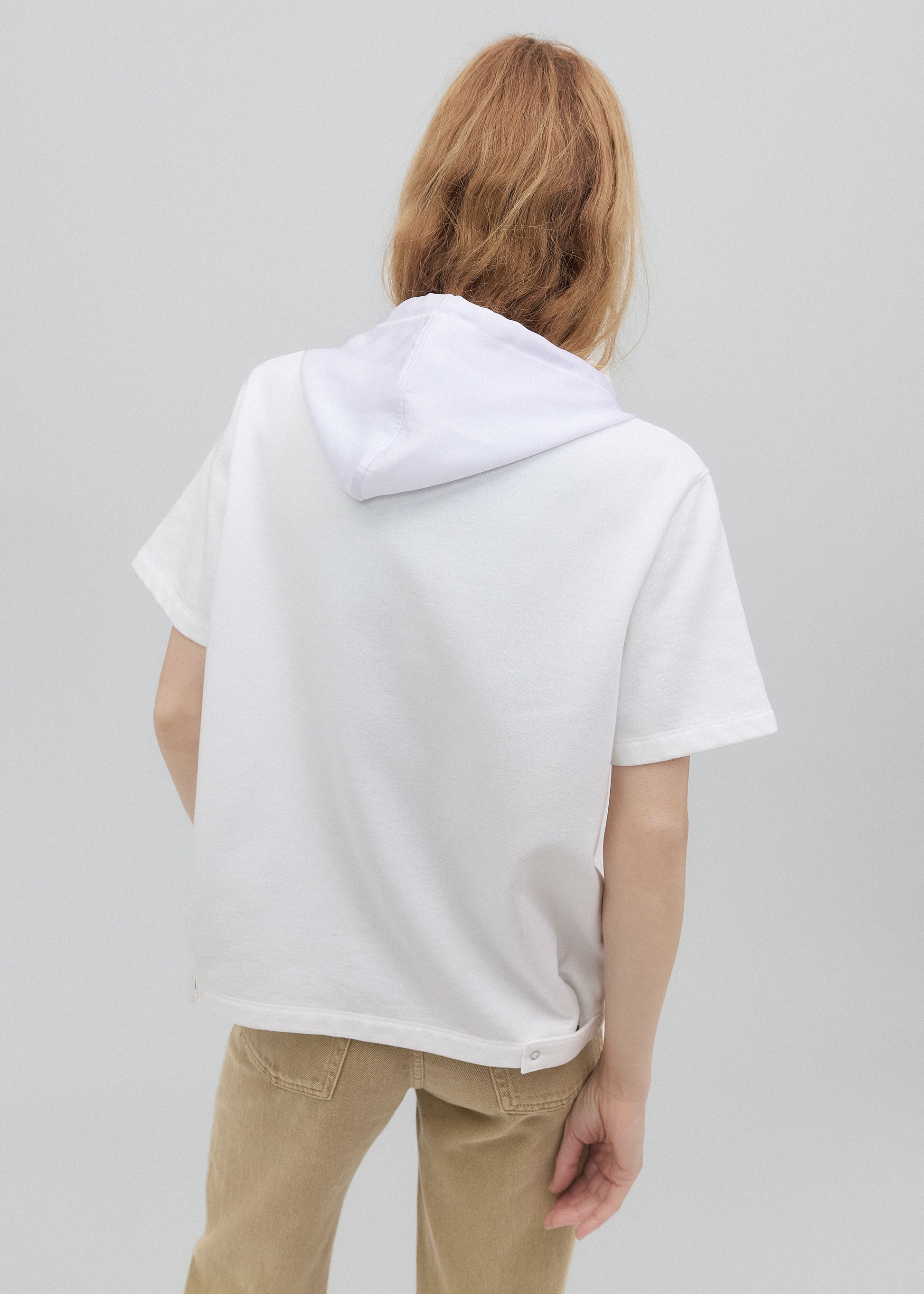 Person wearing a white hoodie and beige pants on a plain background