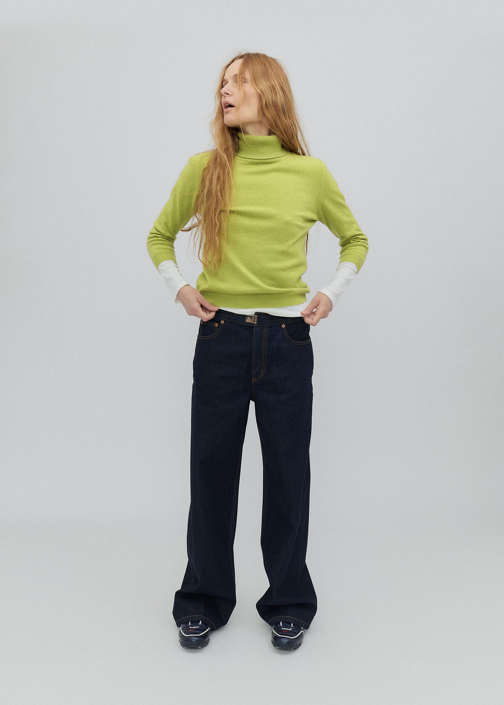 Person wearing a green sweater and black jeans on a plain background