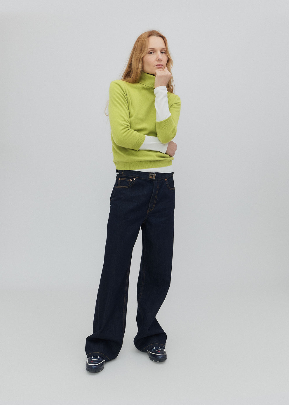 Person wearing a bright green sweater and dark pants on a light gray background