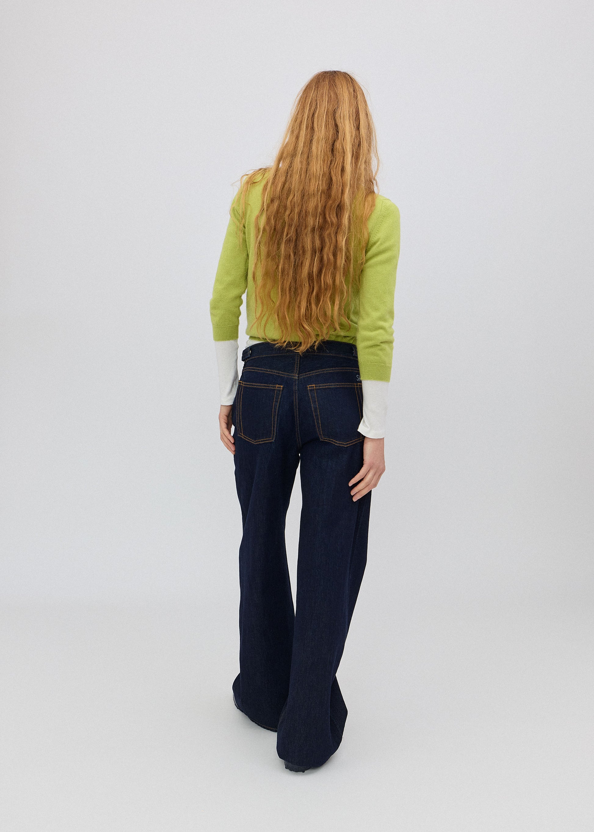 Person wearing a green sweater and dark jeans from behind on a white background