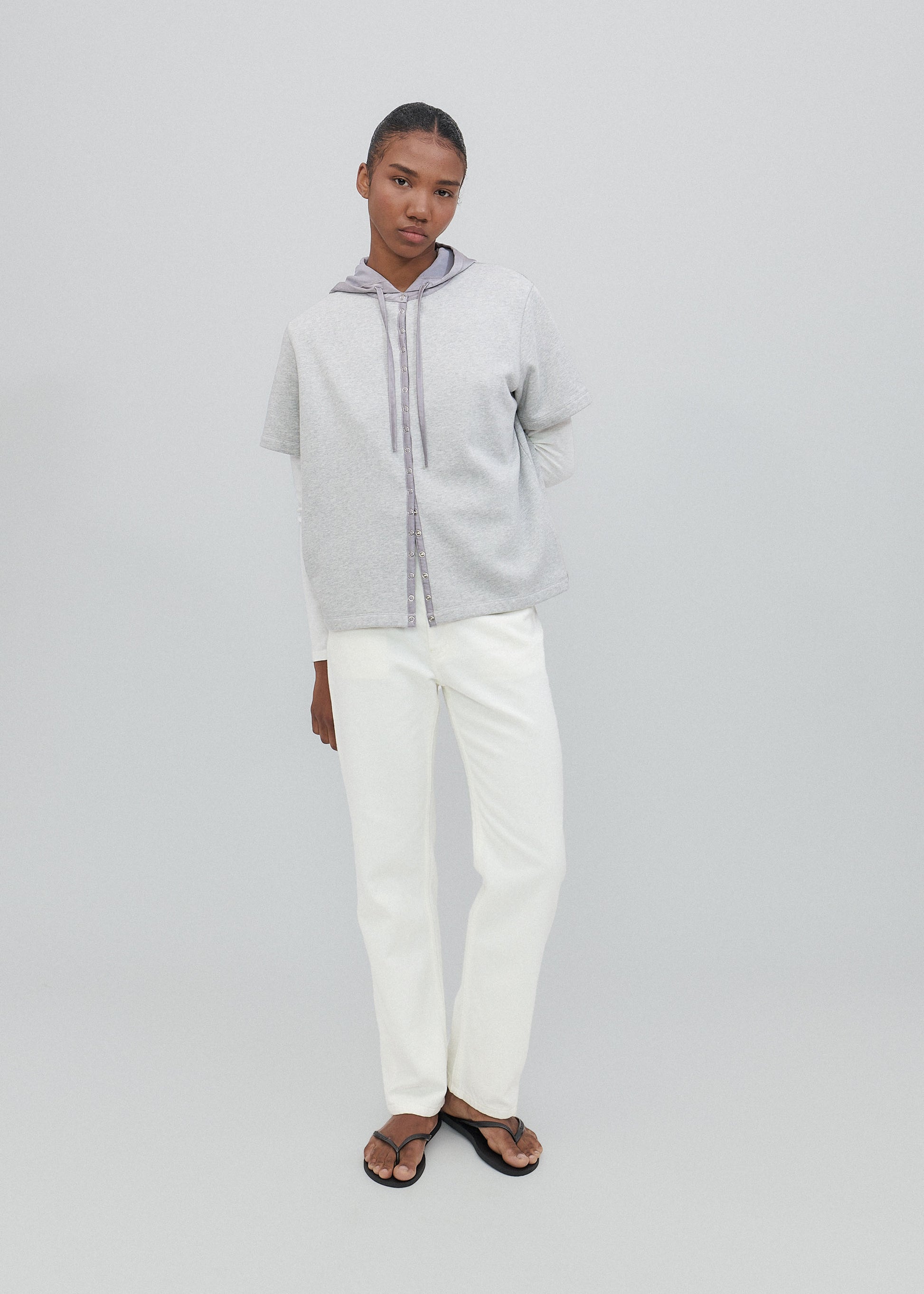 Person wearing a light gray zip-up hoodie and white pants on a plain background
