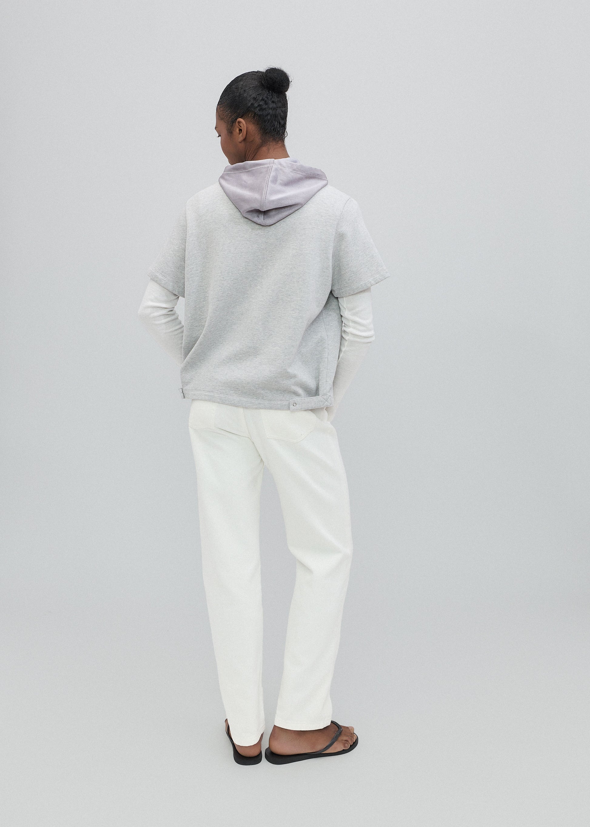 Person wearing a light gray hoodie and white pants on a plain background