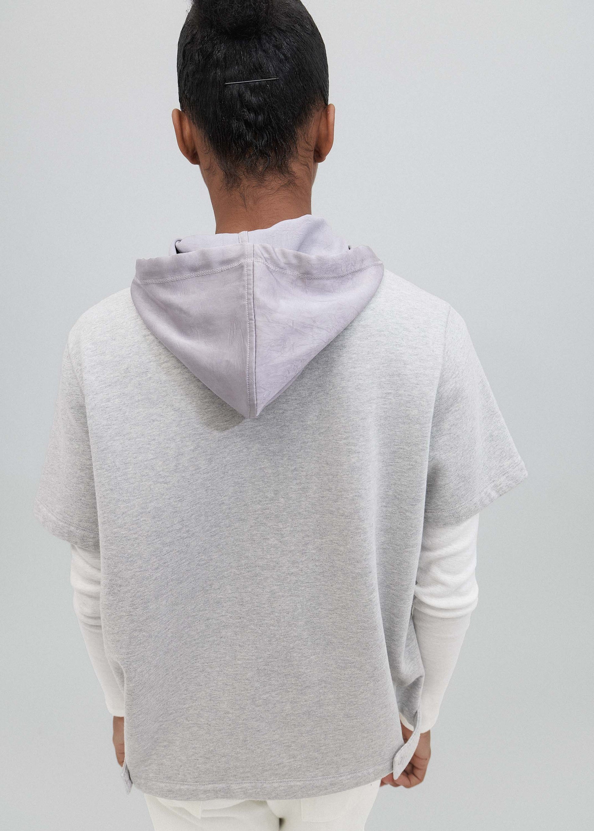 Person wearing a light gray hoodie with a white shirt underneath on a plain background