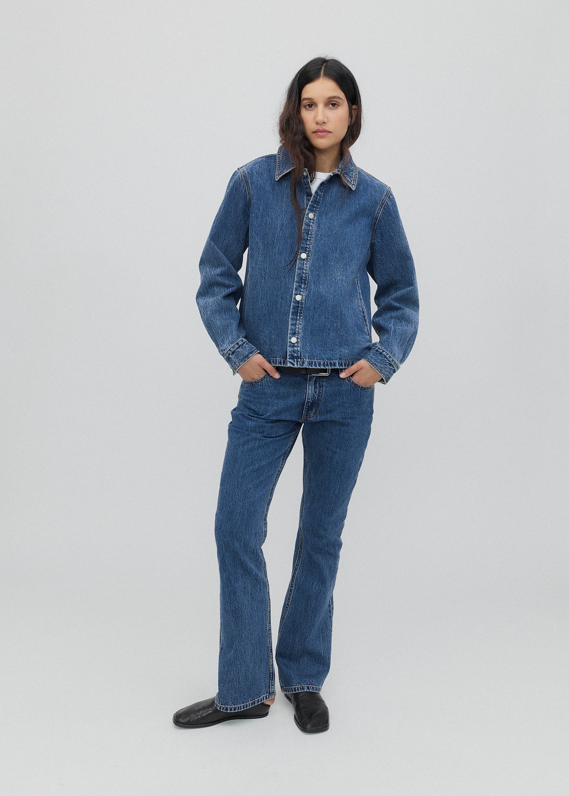 Person wearing a blue denim jacket and jeans on a white background