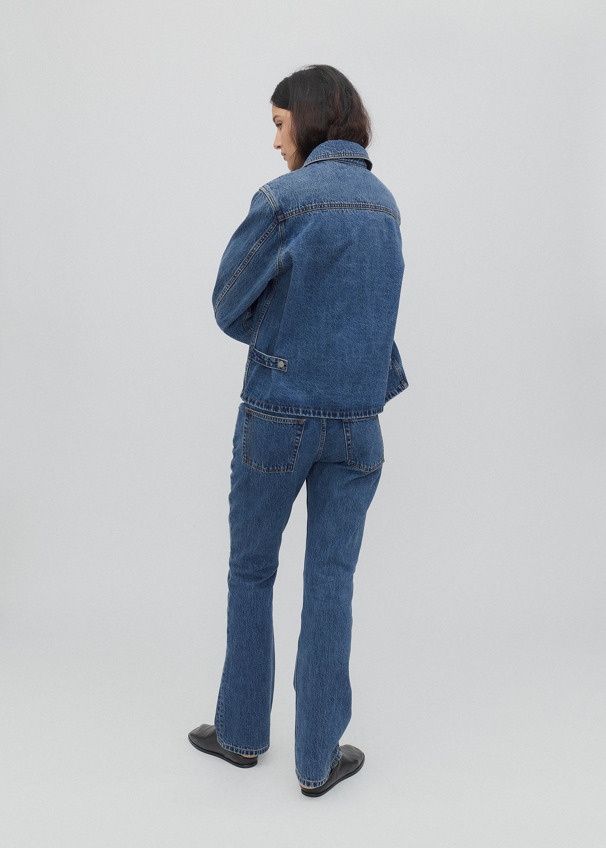 Person wearing a blue denim jacket and jeans on a white background