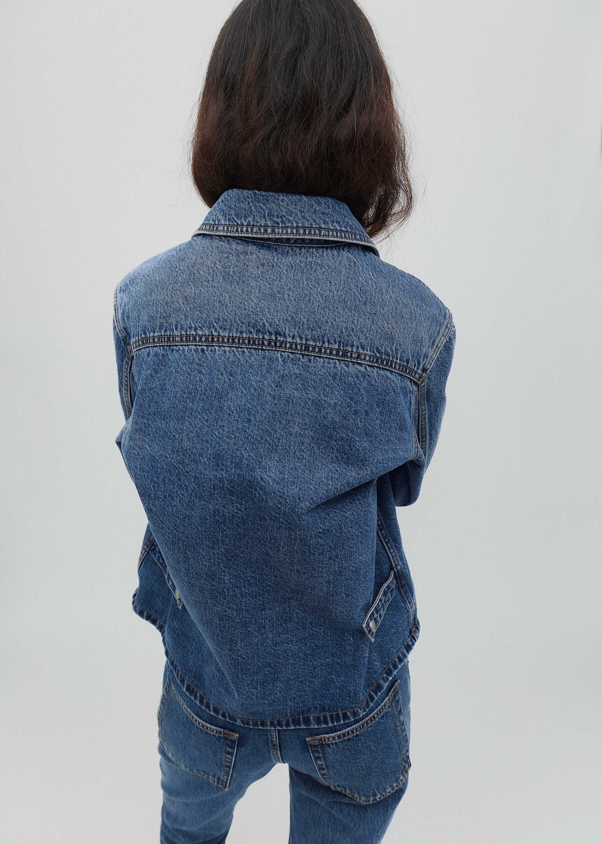 Person wearing a blue denim jacket on a plain background