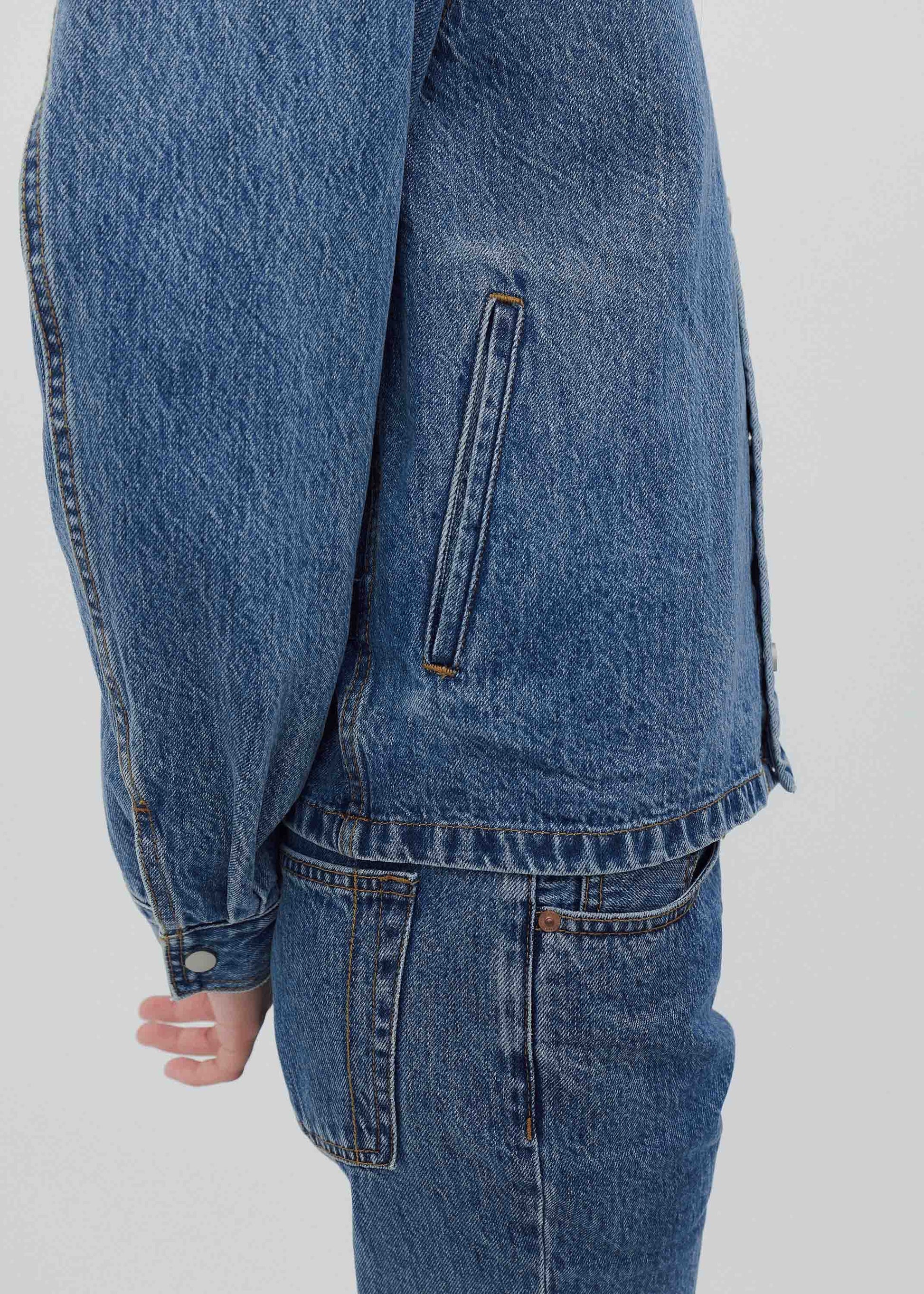 Close-up of a blue denim jacket and jeans on a plain background