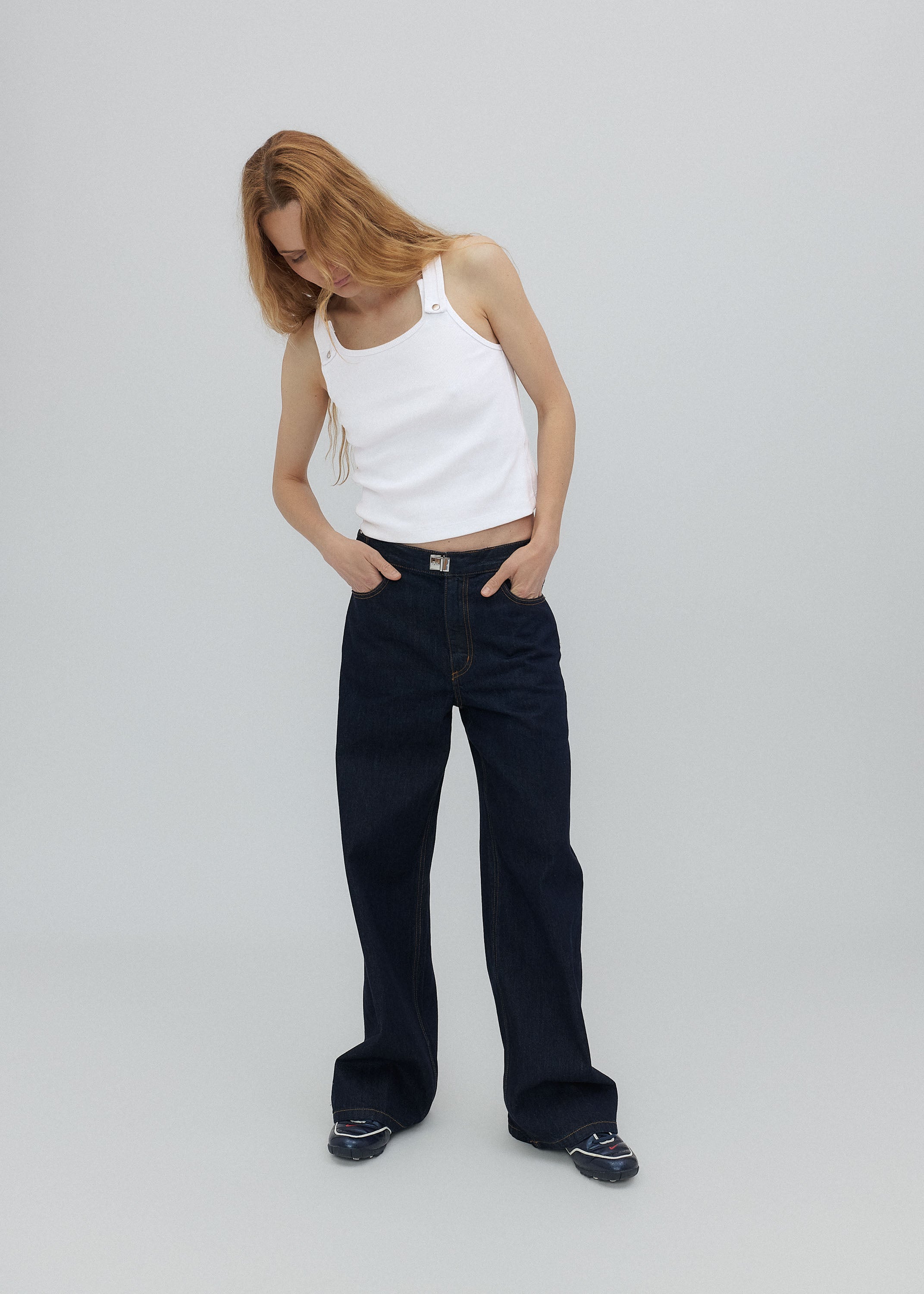 Person wearing a white tank top and black pants on a light gray background