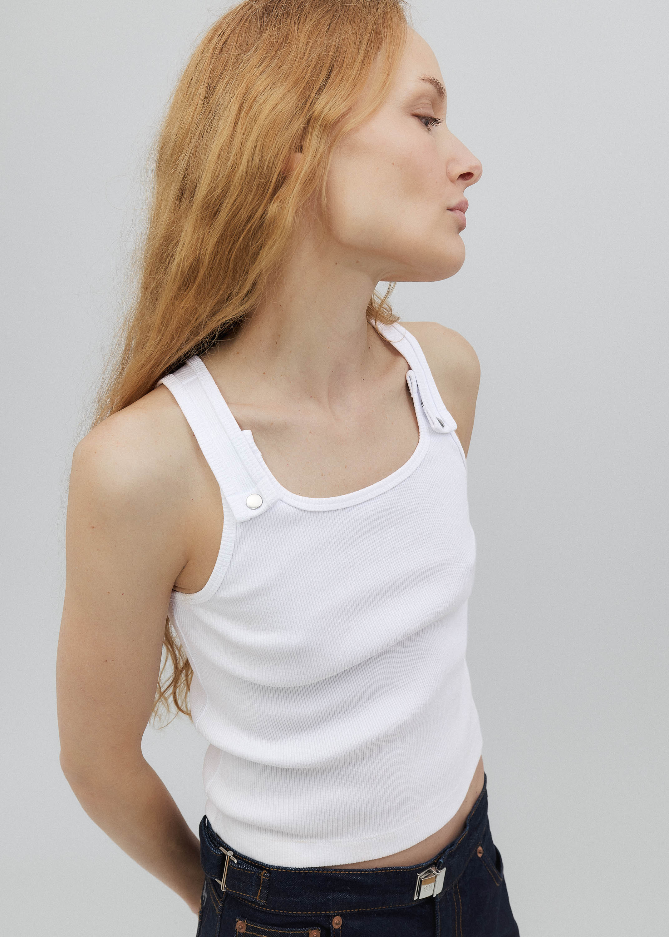 Woman wearing a white tank top against a plain background